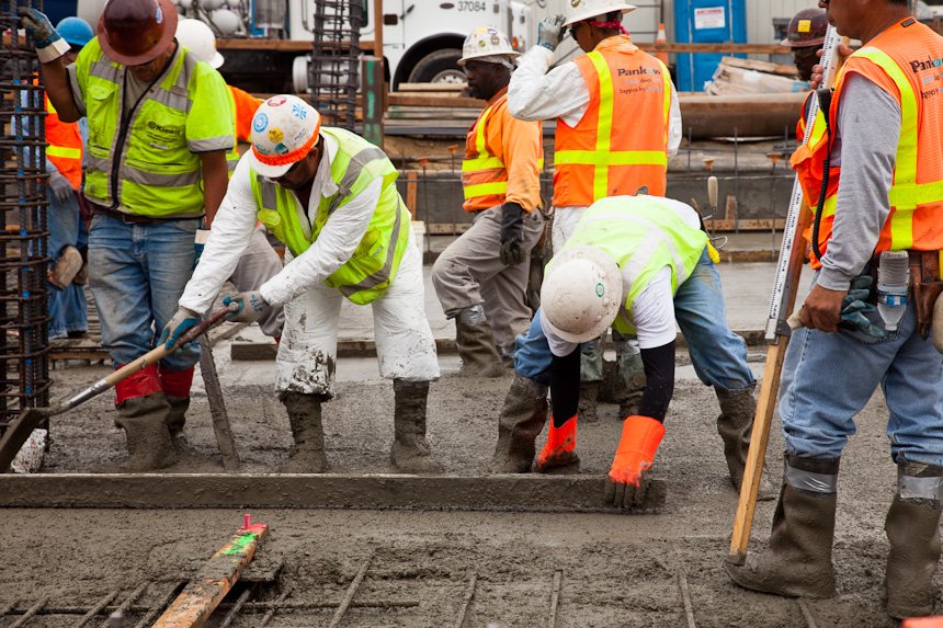 Construction workers pouring and spreading concrete on a building site, wearing safety vests and helmets.