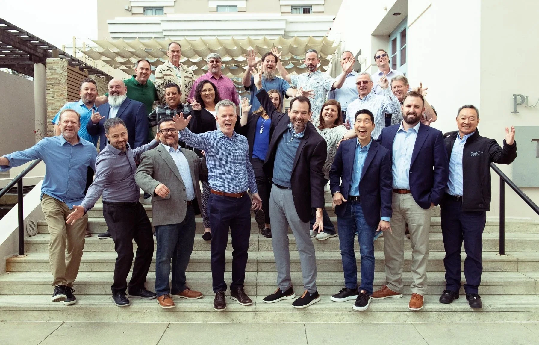 Group of diverse professionals standing and celebrating on outdoor stairs in front of a building.