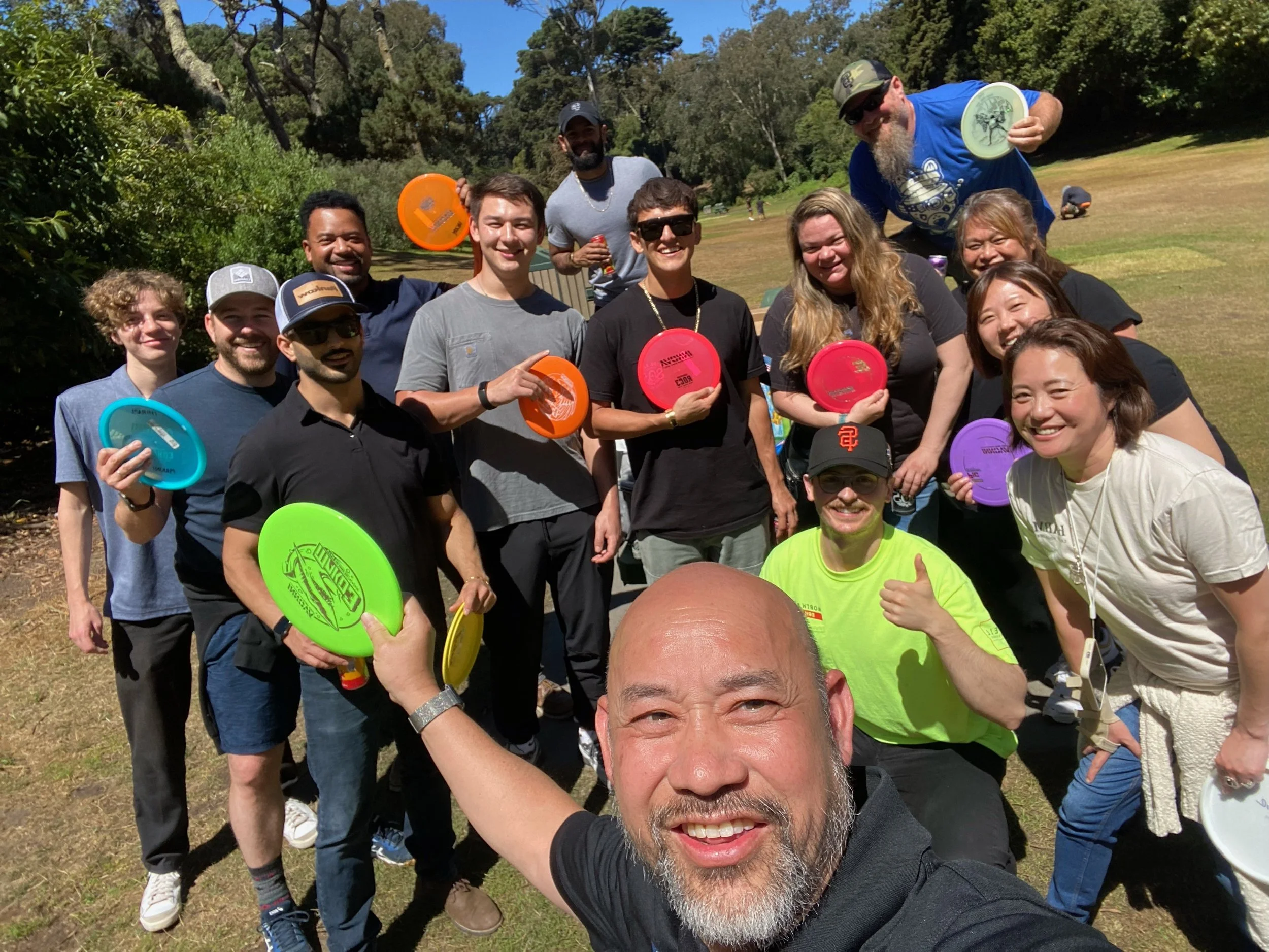 A group of people outdoors on a sunny day holding colorful frisbees, smiling and posing for a photo