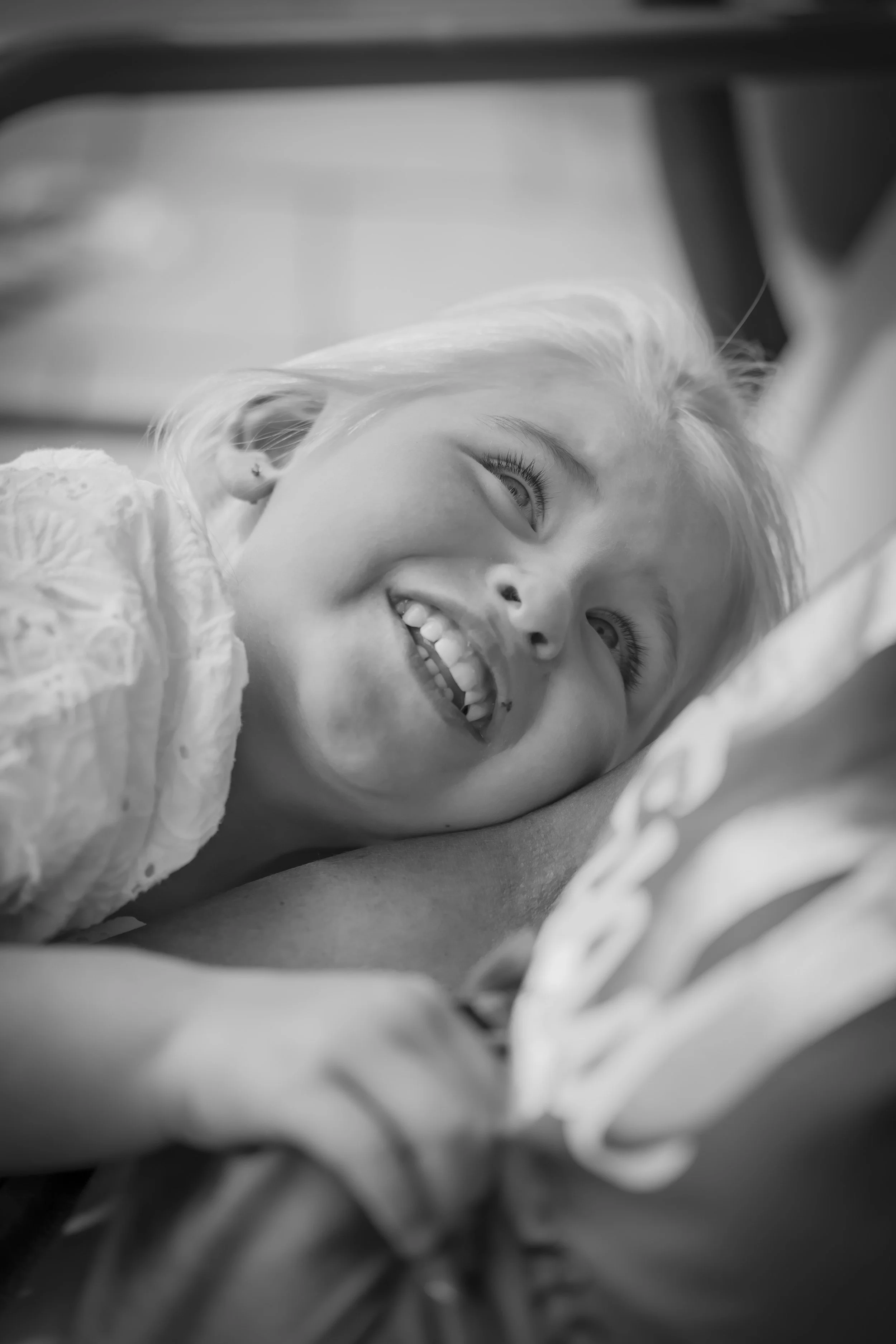 A young girl with blonde hair lying in a hospital bed, smiling and looking up.