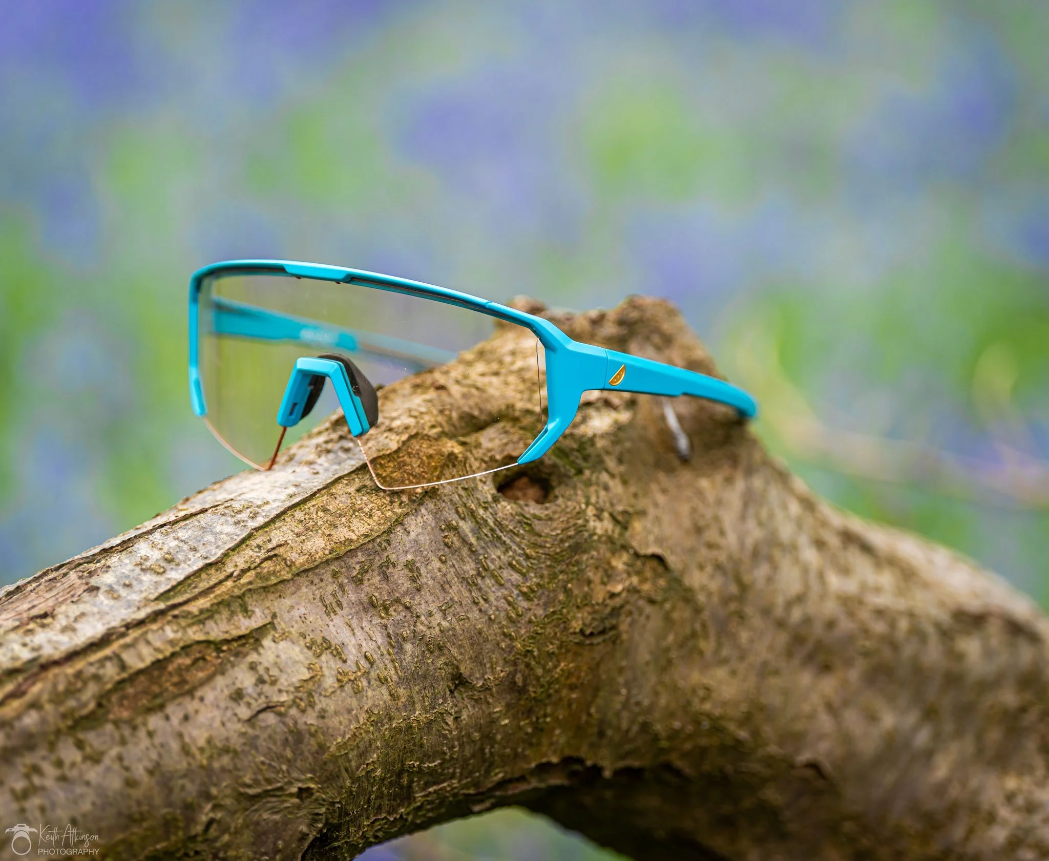 Blue Melon optics sports mountainbike sunglasses resting on a tree branch with green and purple blurred background.