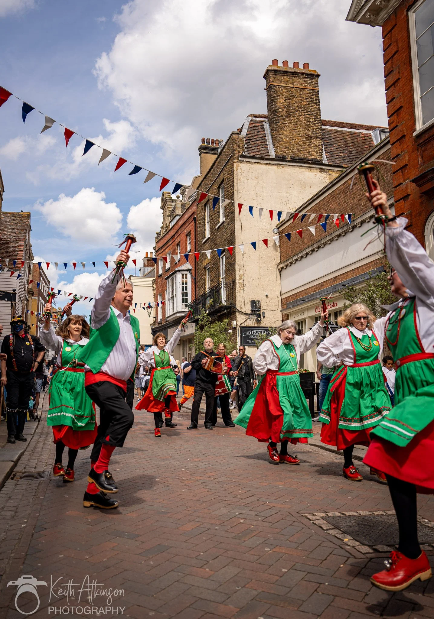 People dressed in colorful costumes performing a traditional dance in a street decorated with triangular banners during a sweeps parade or festival in Rochester Kent.
