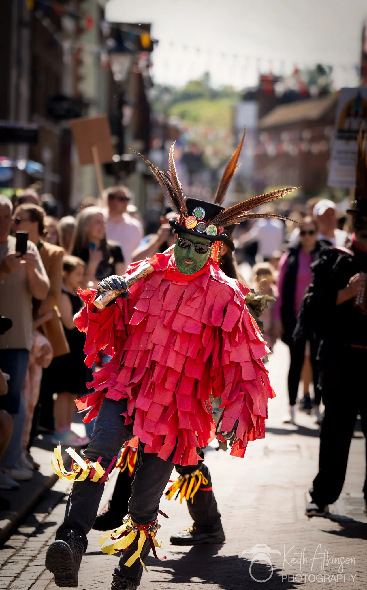 A person dressed in a colorful costume participating in a street festival or parade, surrounded by spectators and onlookers.