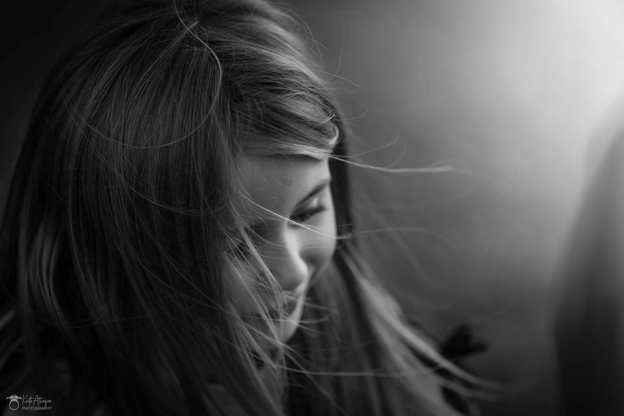 Close-up black and white photo of a woman's face in profile with her hair flowing. She is looking downward.