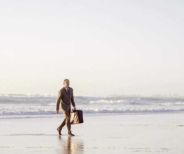 A person walking along the beach with a suitcase during daytime