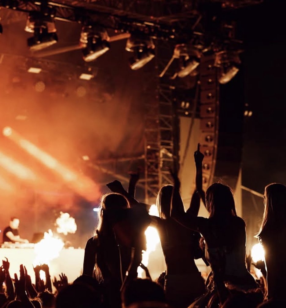 People dancing at a concert with bright stage lights and smoke effects.