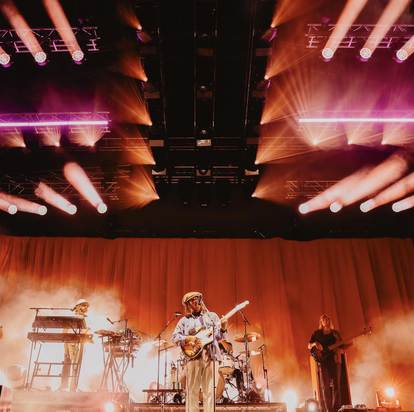 A live music performance on stage with band members, colorful lighting, and smoke effects.
