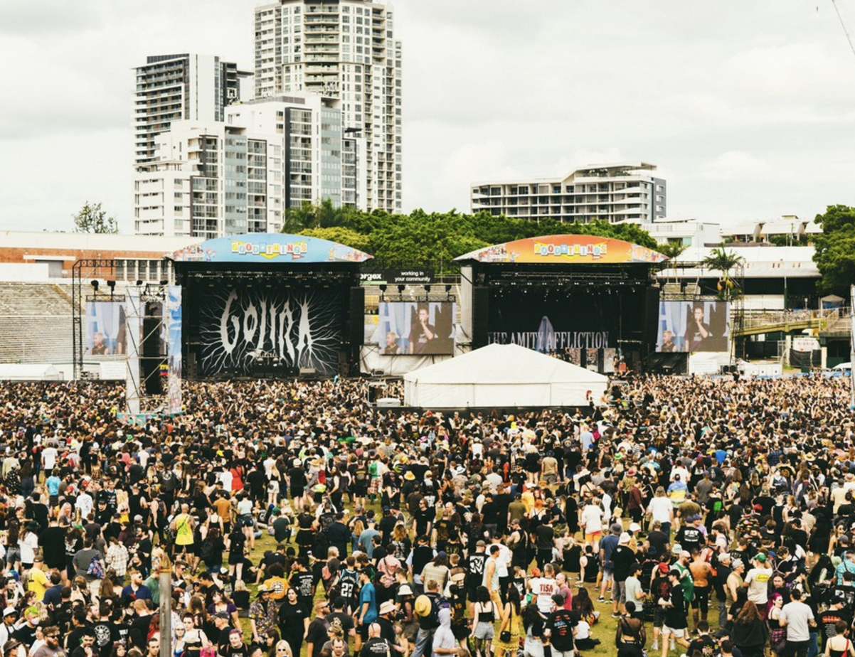 Large outdoor music concert with a big crowd, stage, performers, and screens in front of tall apartment buildings.