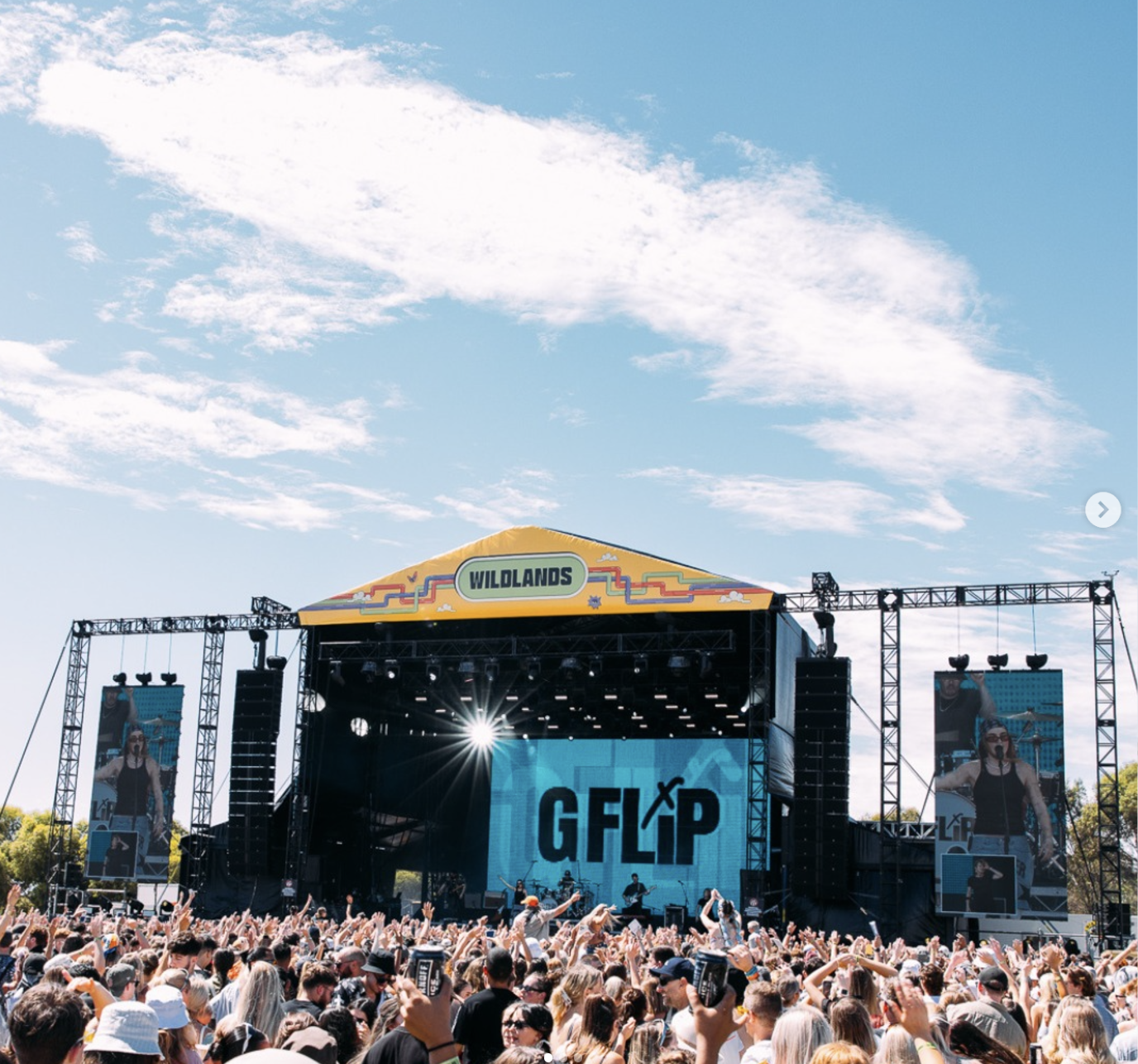 Outdoor music festival with a large crowd in front of a stage labeled 'GF∆P' and 'WILDLANDS' under a blue sky with clouds.