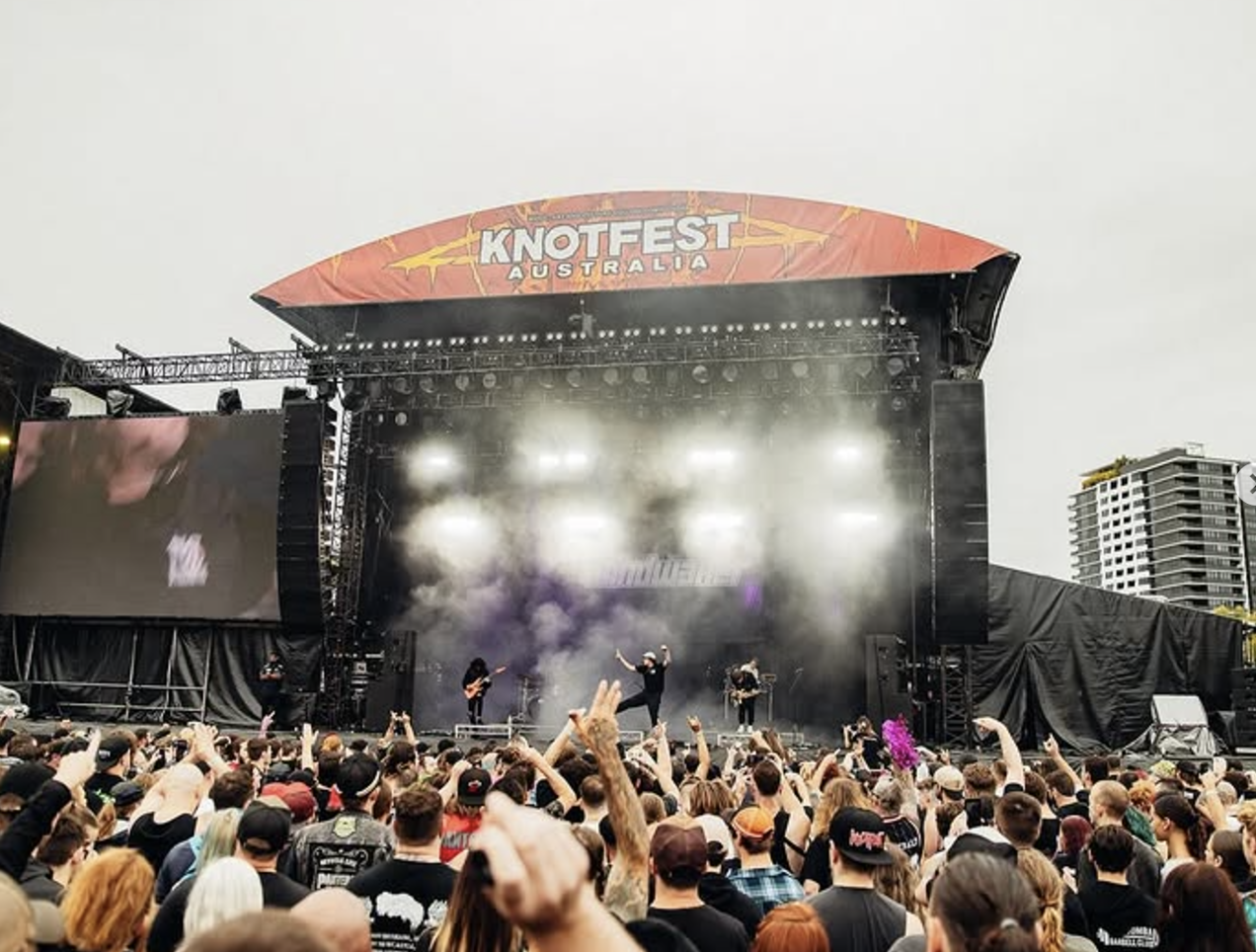 Crowd attending a live rock concert at Knotfest Australia with a band performing on stage and drums in the background.