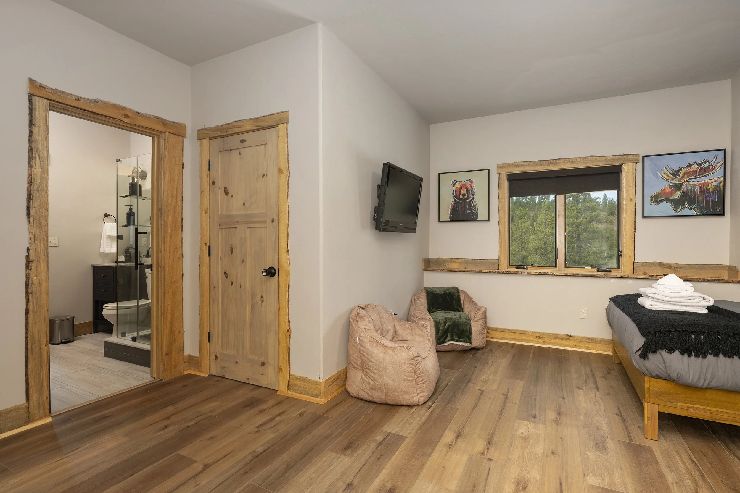 Bunk bedroom with a wall-mounted TV, two plush chairs, and art pictures of a bear and a moose, with a visible bathroom through an open door.