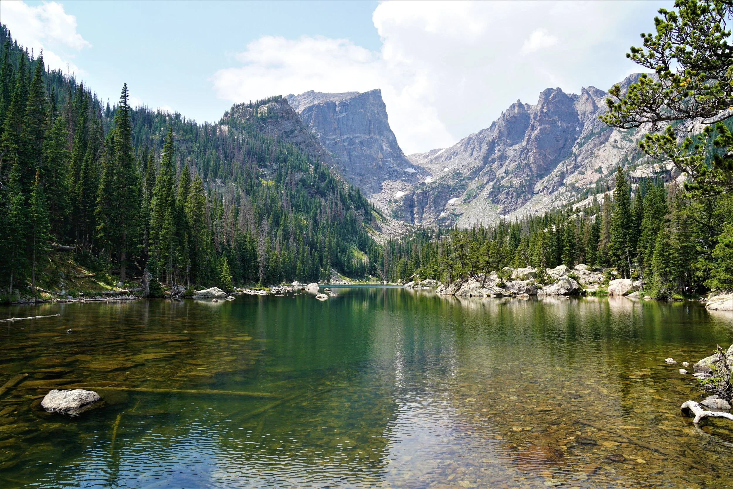 A scenic view of a mountain lake surrounded by evergreen trees and tall rocky mountains under a partly cloudy sky.