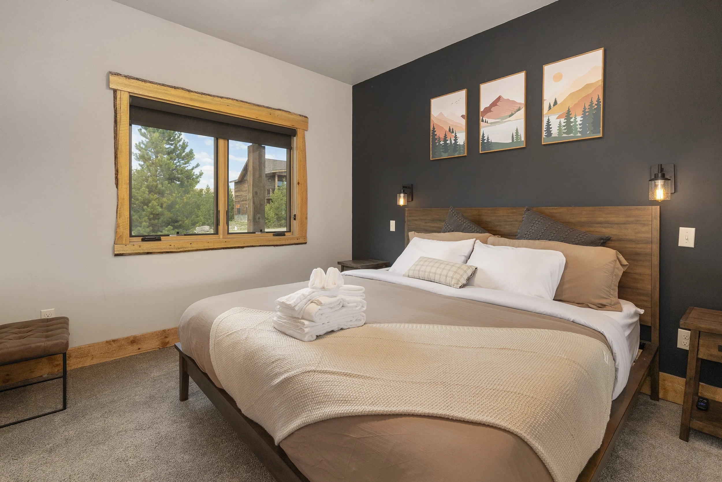 Upstairs master bedroom with a wooden bedframe, beige bedding, and pillows. Sconces on either side of the bed. Mountain landscape artwork above the headboard.