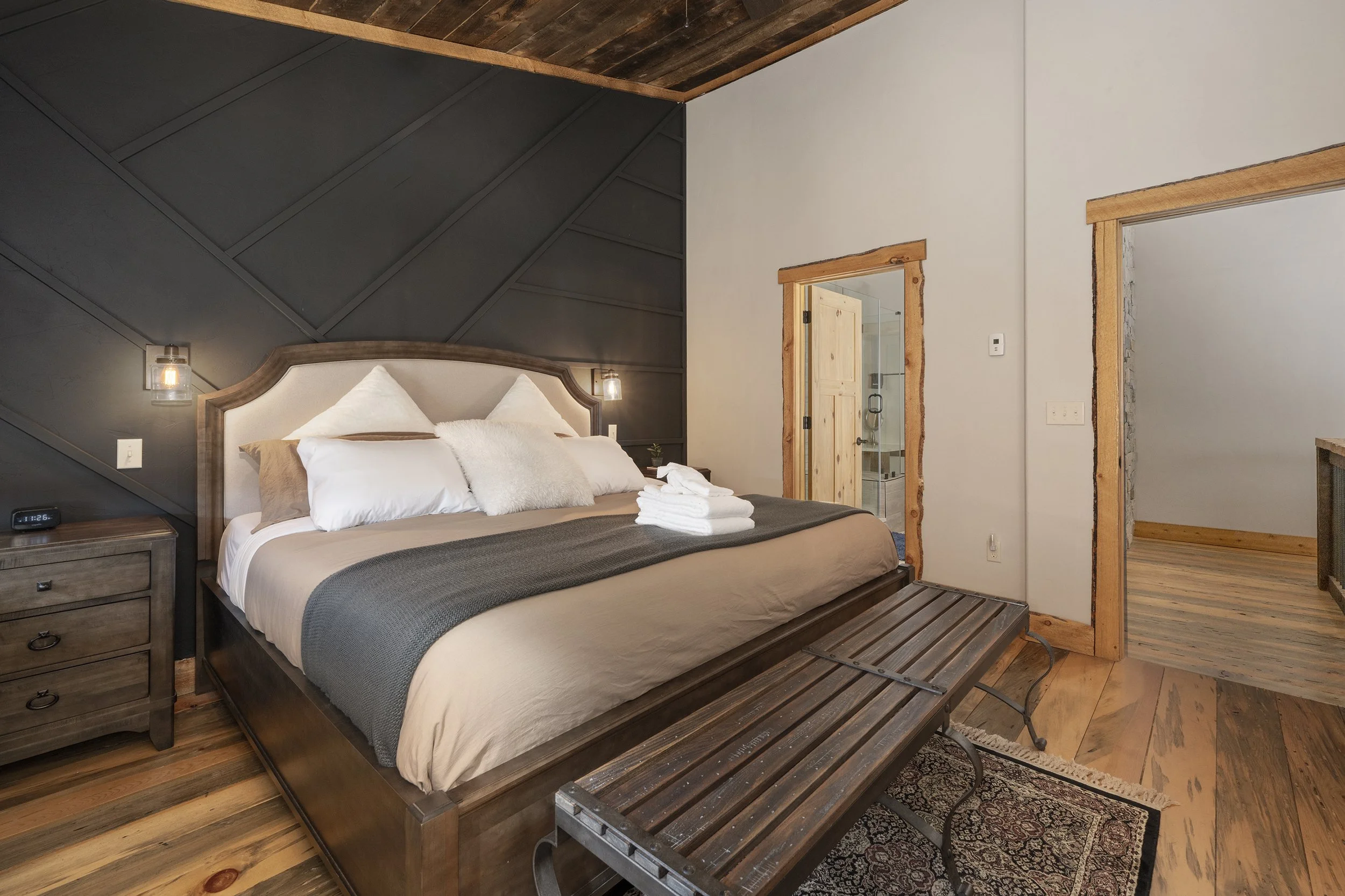 Master bedroom with a king bed, dark and light wood accents, and a view of a bathroom through an open door.