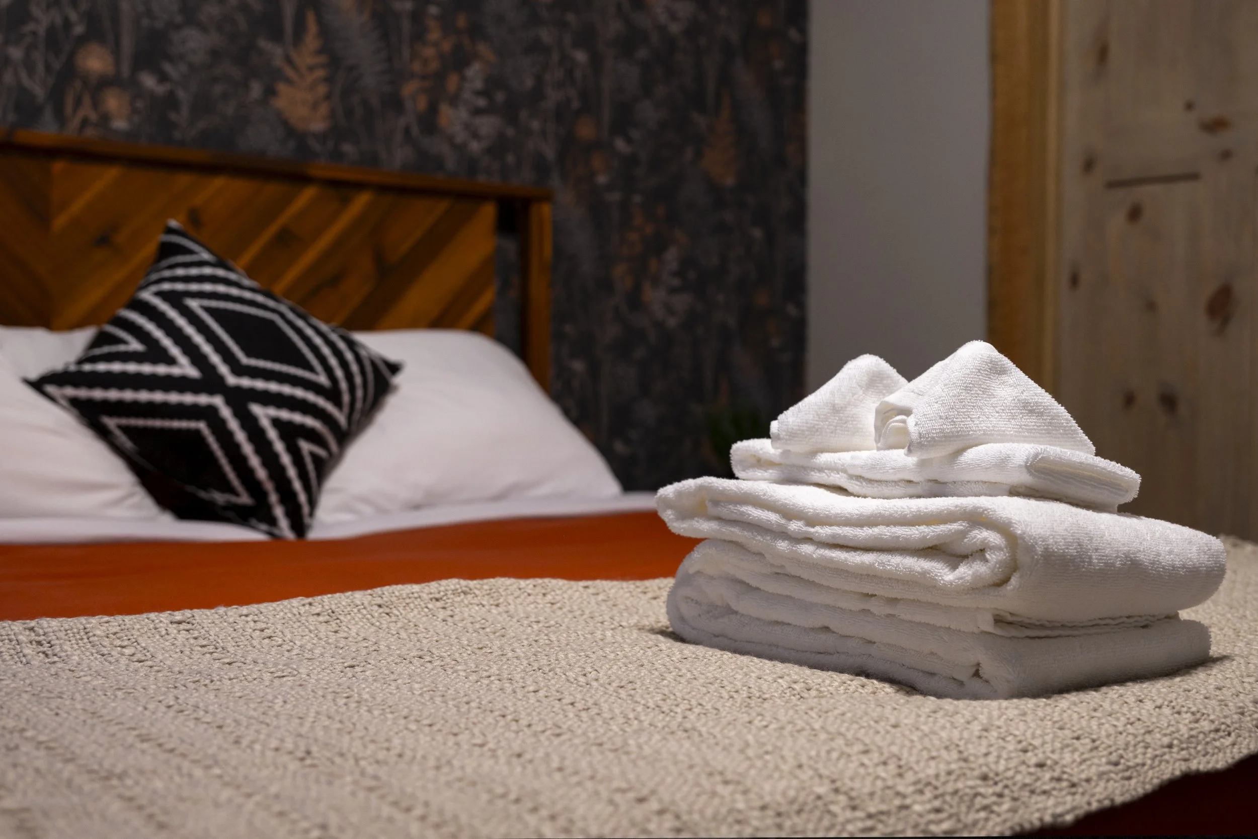 Basement king bedroom at Rocky Heart Hideaway chalet in Grand Lake, CO, featuring white linens, wooden headboard, cozy dark wallpaper, and neatly folded white towels.