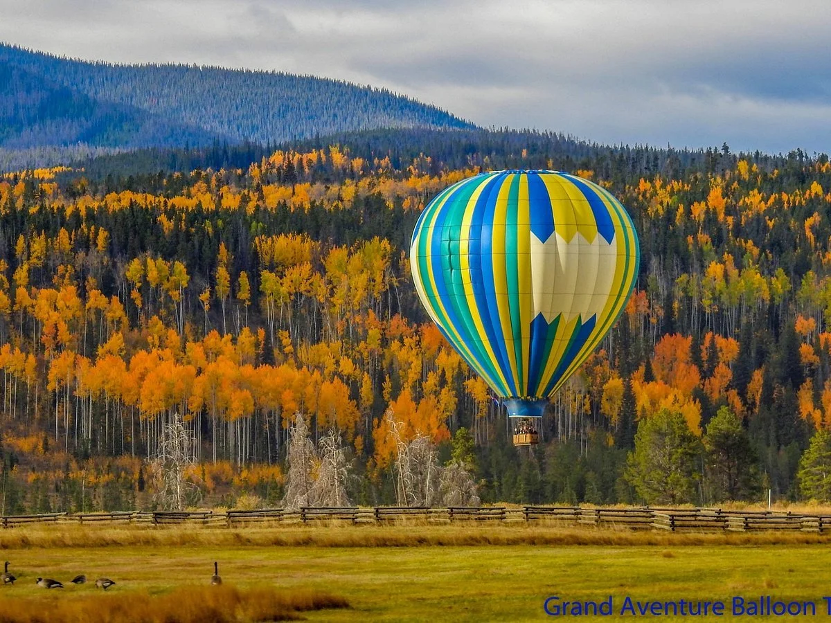 A colorful hot air balloon flying over an autumn landscape with trees in fall colors and mountains in the background.