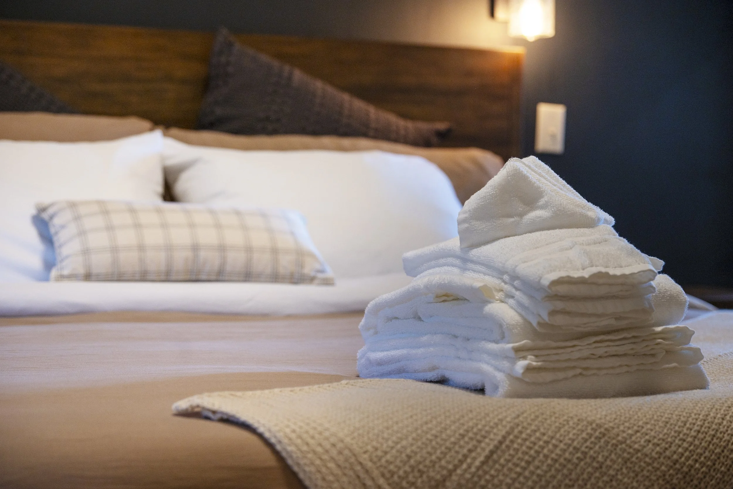 Neatly folded white towels on the bed in the master bedroom of Rocky Heart Hideaway chalet, with beige bedding, wooden headboard, and soft ambient lighting in Grand Lake, CO.