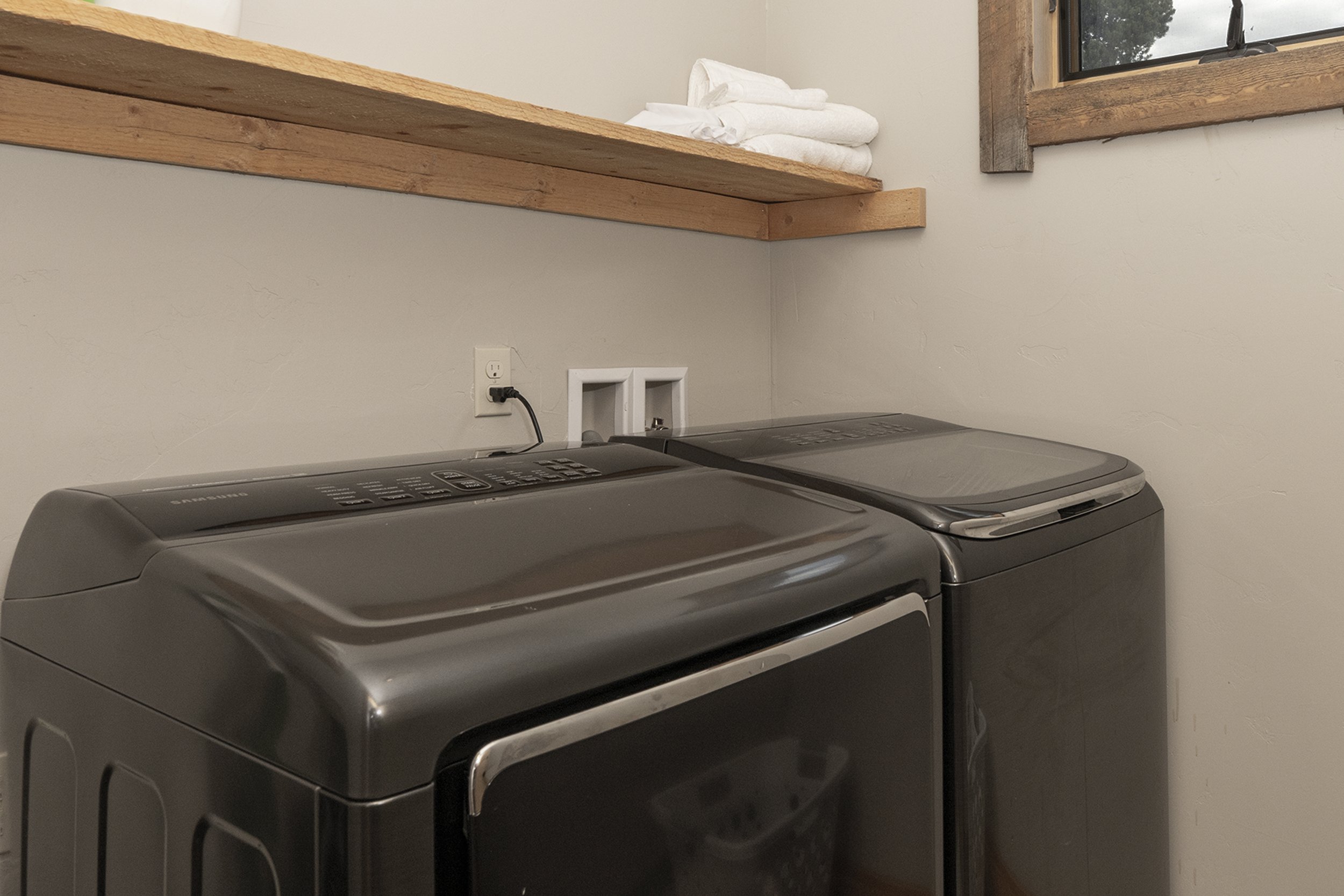 A laundry room with a washer and dryer, a wooden shelf with folded towels, and a window.