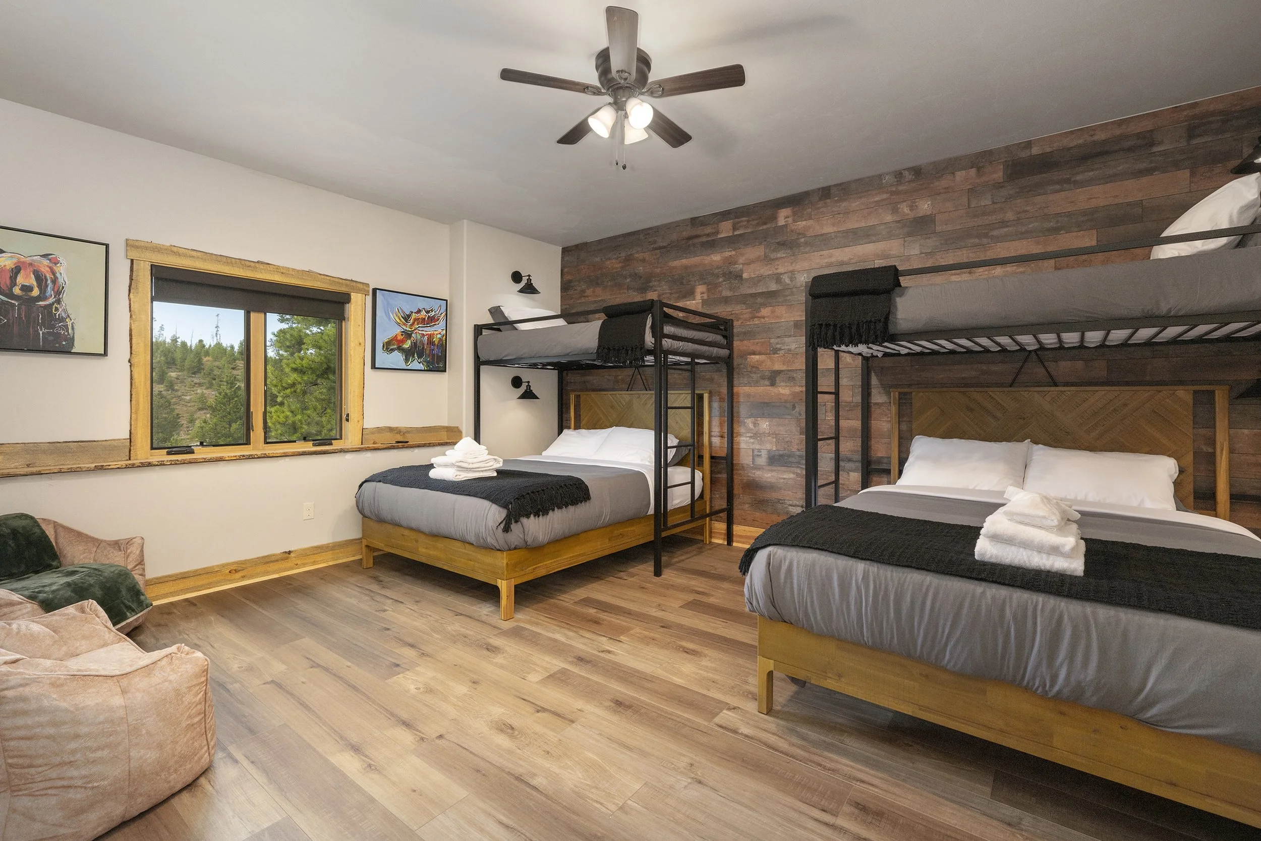Bunk room with two beds, each with a bunk bed on top, wooden floors, a window with mountain view, and artworks of bears and a moose on the wall.