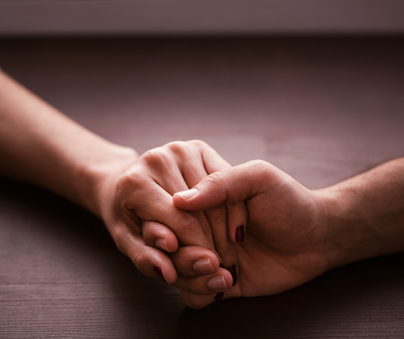 Close-up of a man and woman's hands holding each other gently on a wooden surface.