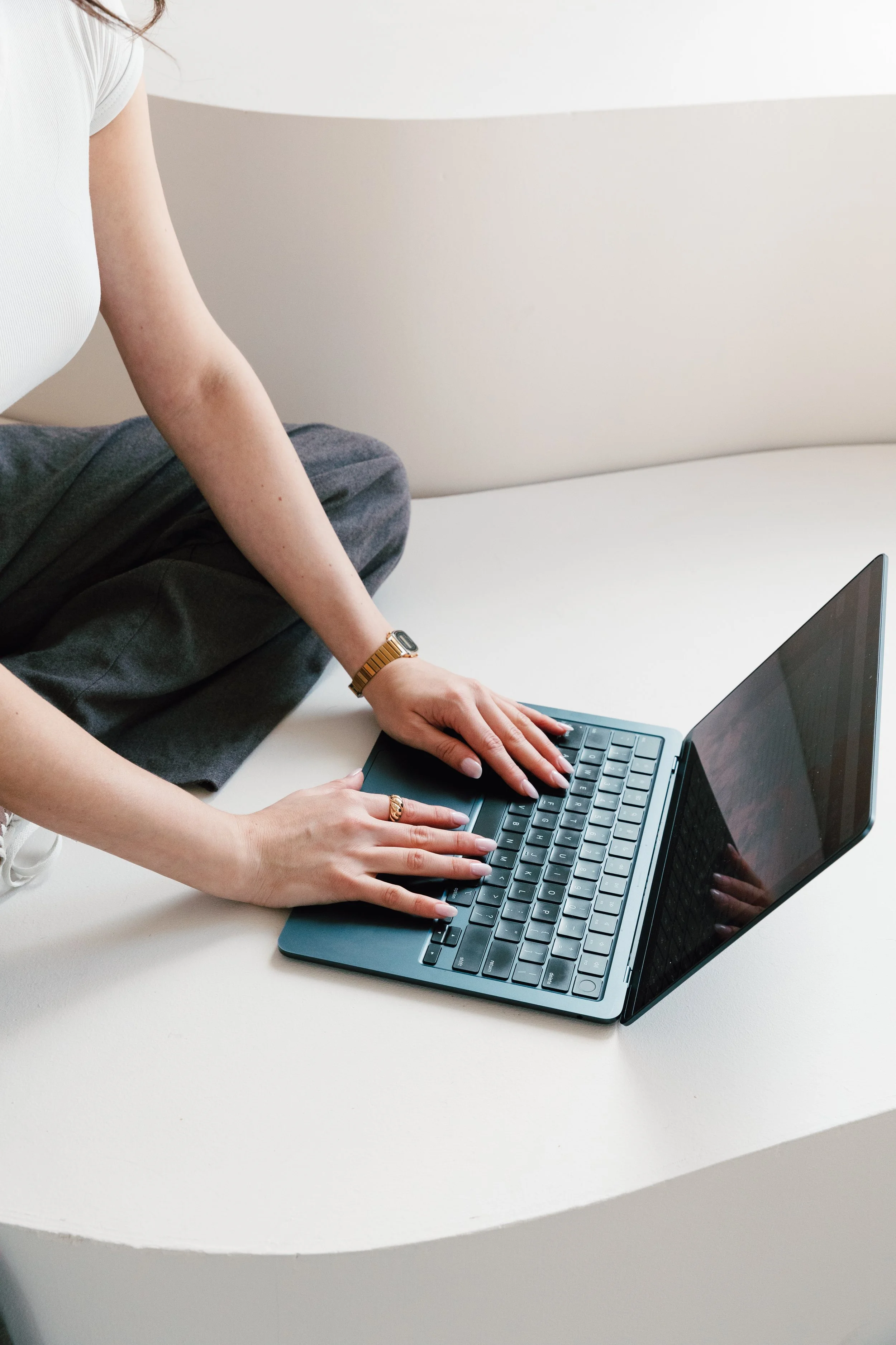 Person sitting cross-legged on a white surface typing on a laptop.