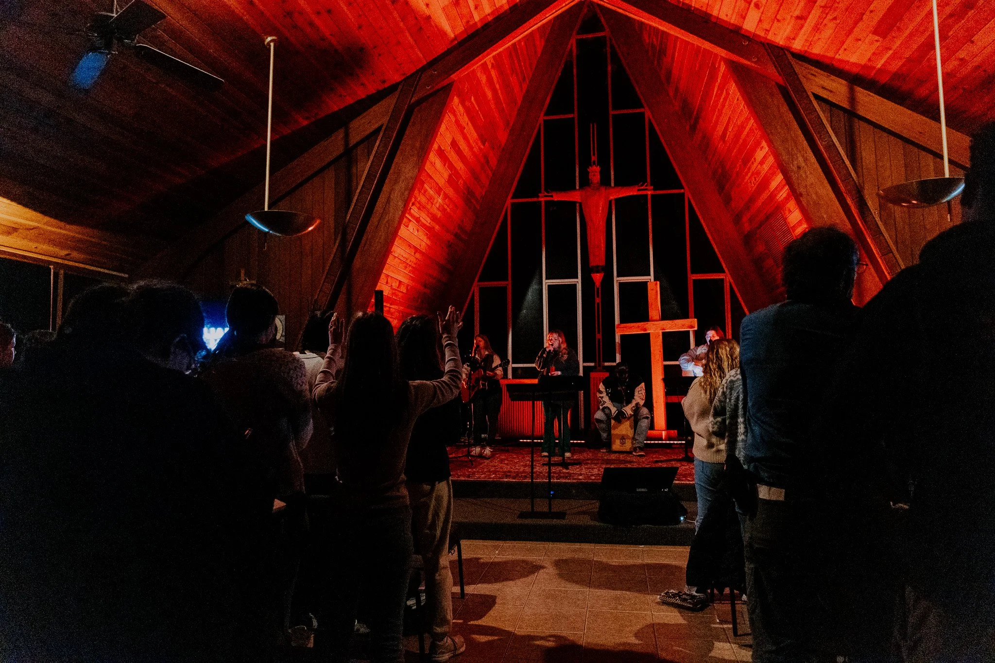 People attending a worship service inside a church, with a cross and a crucifix visible at the altar, while a band performs music in front of the congregation.