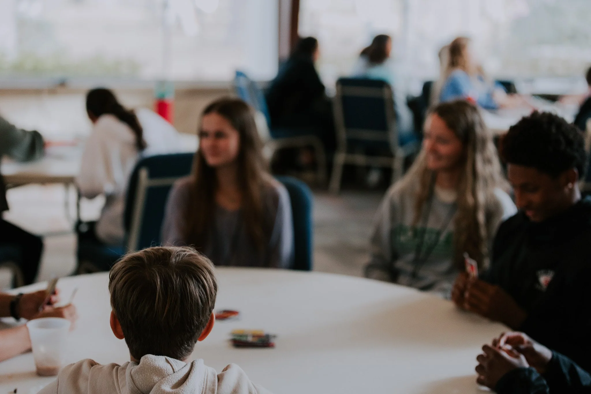 People playing a card game at a round table in a classroom or community center.