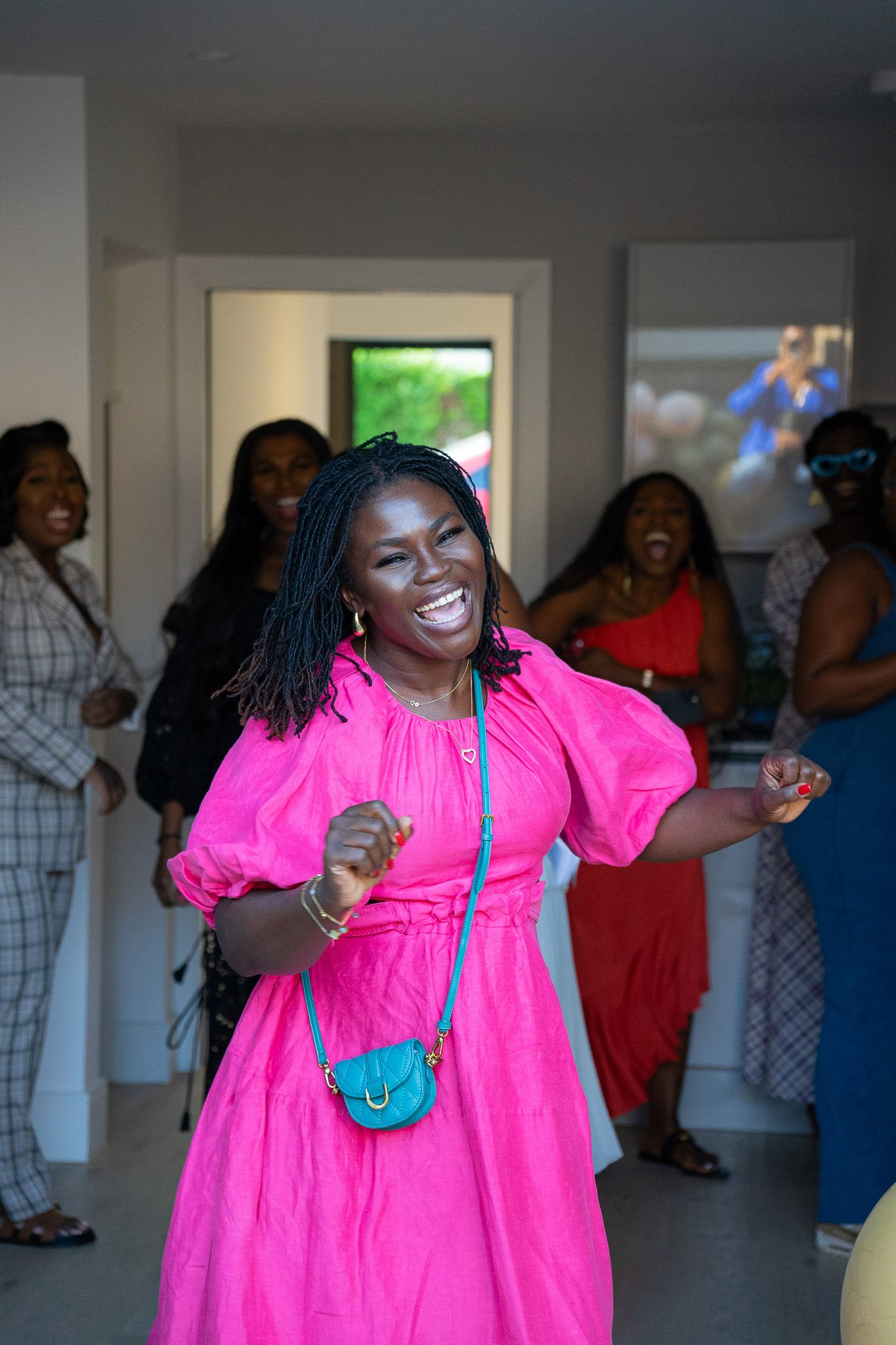 A woman in a pink dress is smiling and dancing at a celebration, surrounded by other women.