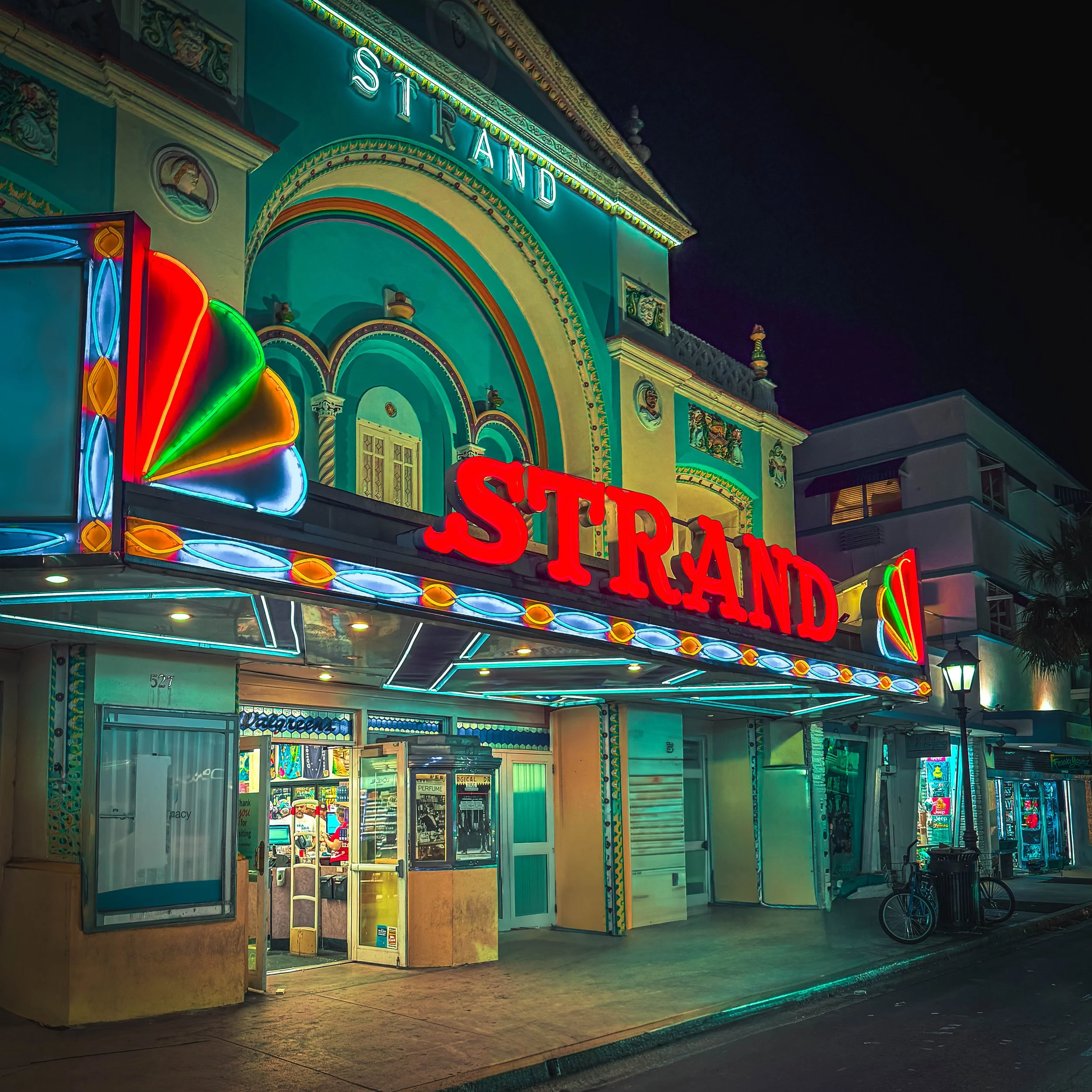 Night view of a colorful, illuminated casino or entertainment venue with neon lights and signs, including a partial view of the word 'STARD'. The building features decorative architectural elements and a street scene with a bicycle parked outside.