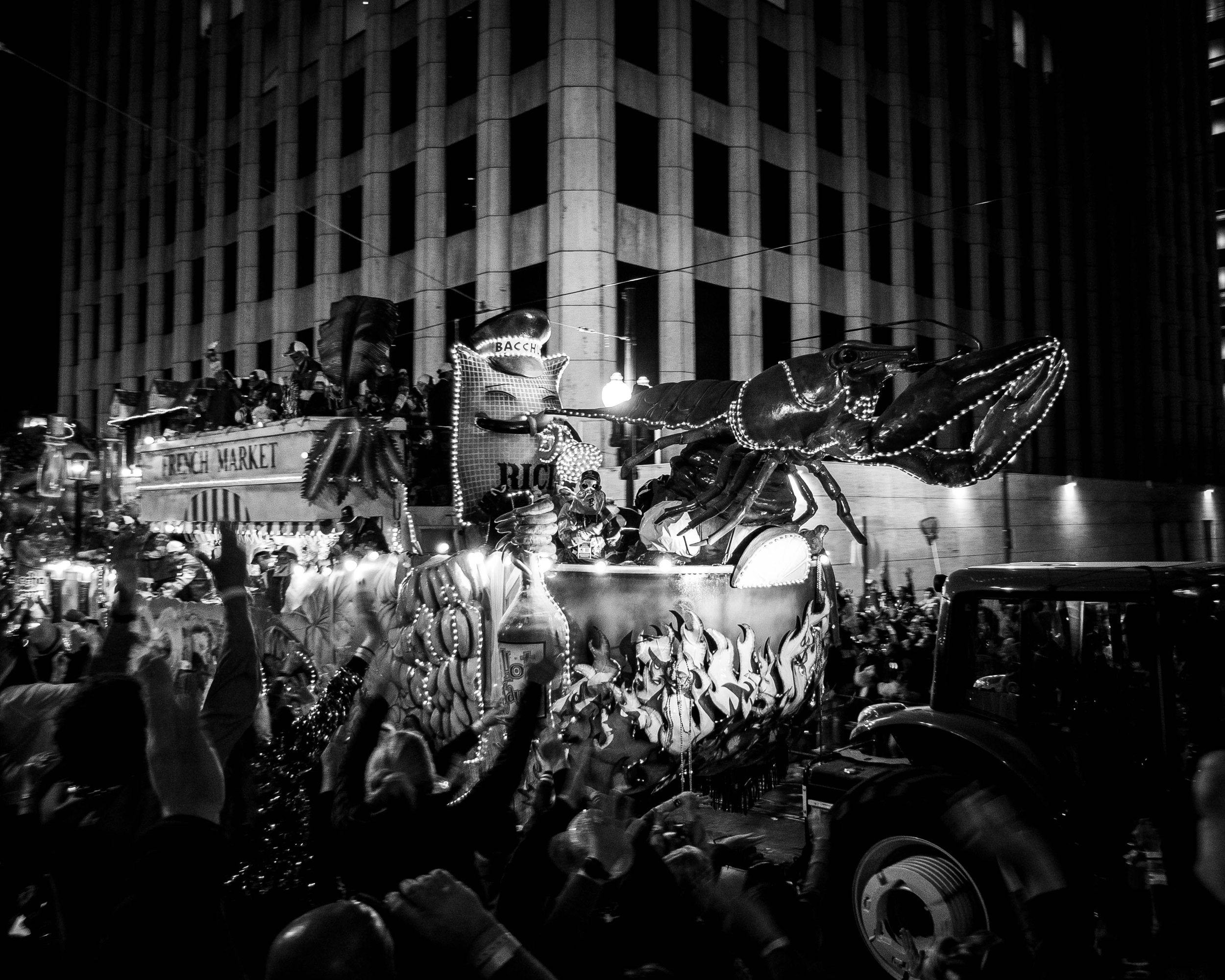 Night scene of a parade float with a large lobster sculpture decorated with lights, appearing in front of a tall, patterned building.