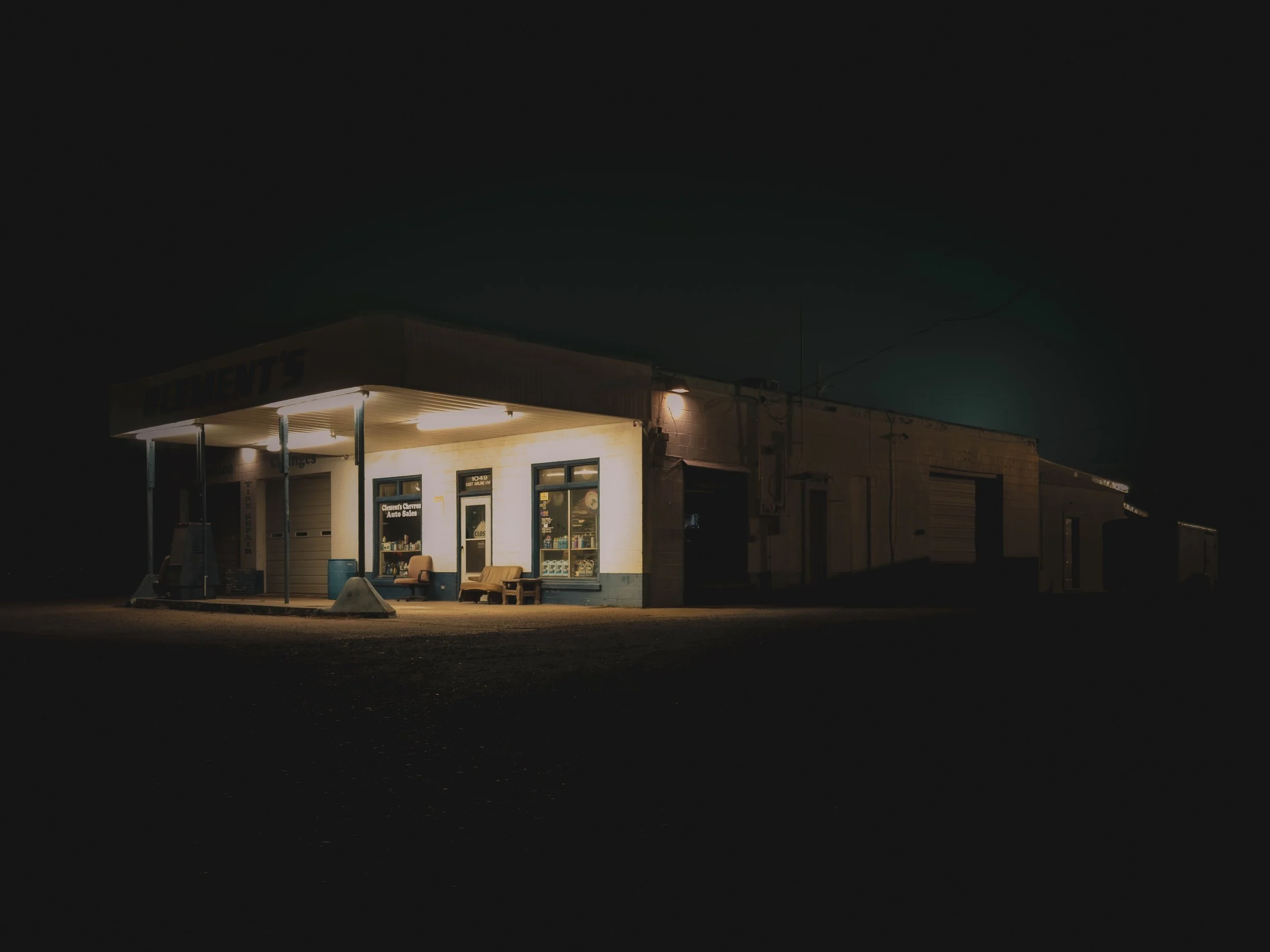 A small, illuminated storefront at night with a sign that reads 'ELEMENT'S' and seating outside, surrounded by darkness.