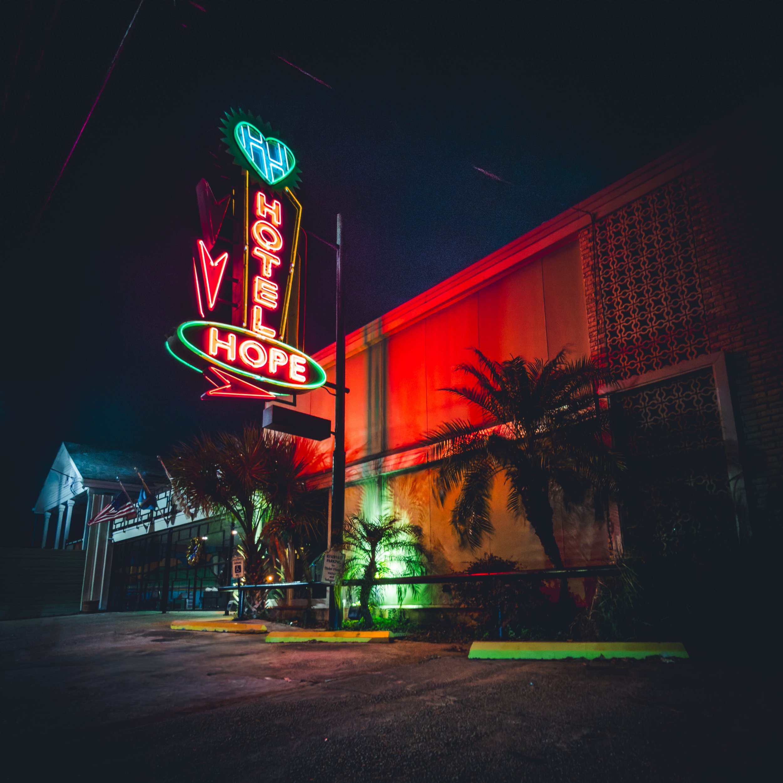 Nighttime neon sign reading 'Hope' with colorful lighting and palm trees in front of a building.