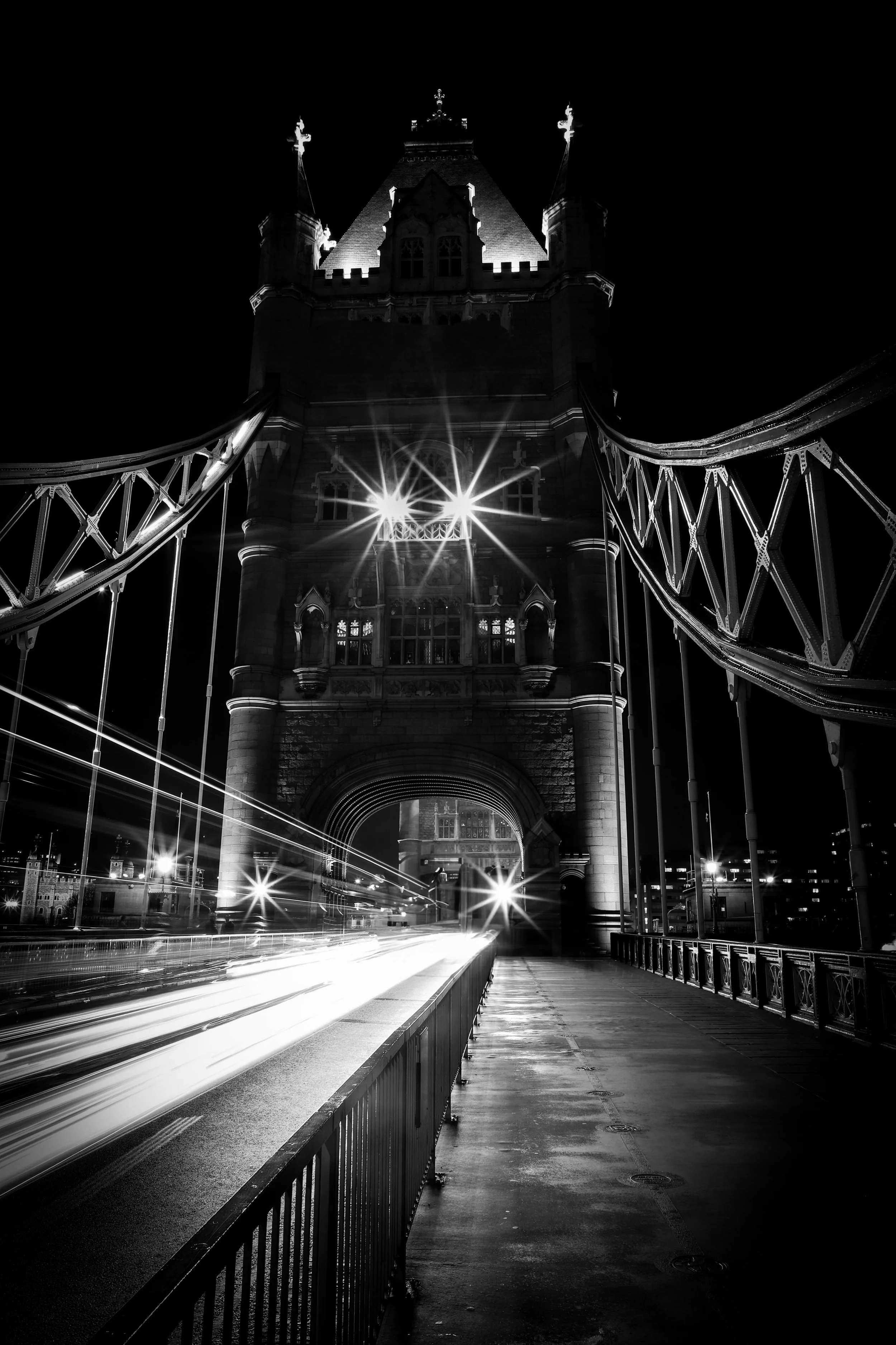 Night view of Tower Bridge in London with light trails from moving vehicles, illuminated bridge towers, and dark sky.