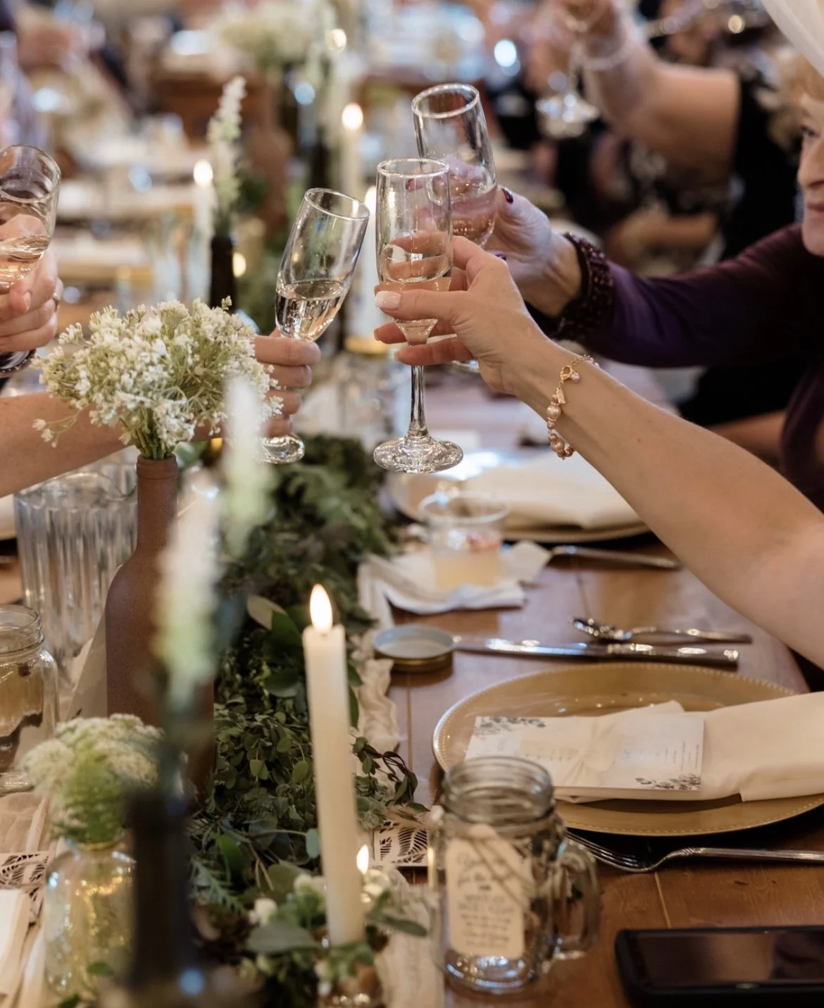 People raising glasses of champagne at a decorated dinner table with floral arrangements and candles.