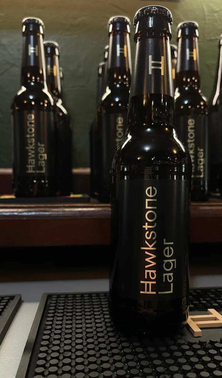 Bottles of Hawkstone Lager displayed on the bar at The Dun Cow, showcasing the pub's drinks selection in Hornton, Oxfordshire.