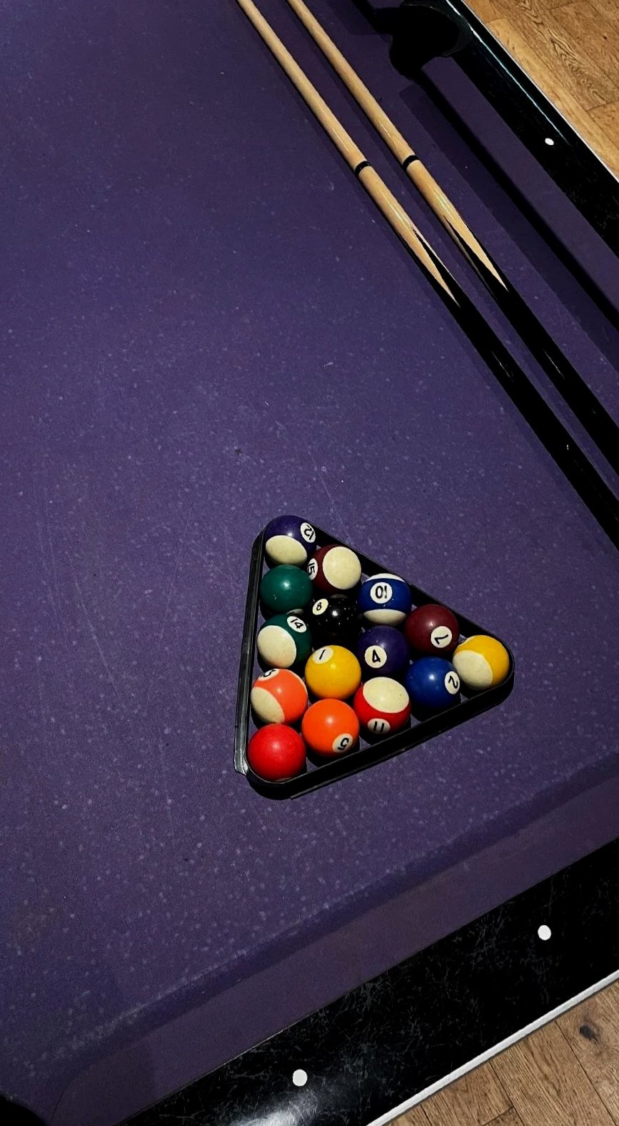 A pool table with a triangular rack of coloured billiard balls in The Dun Cow games room.