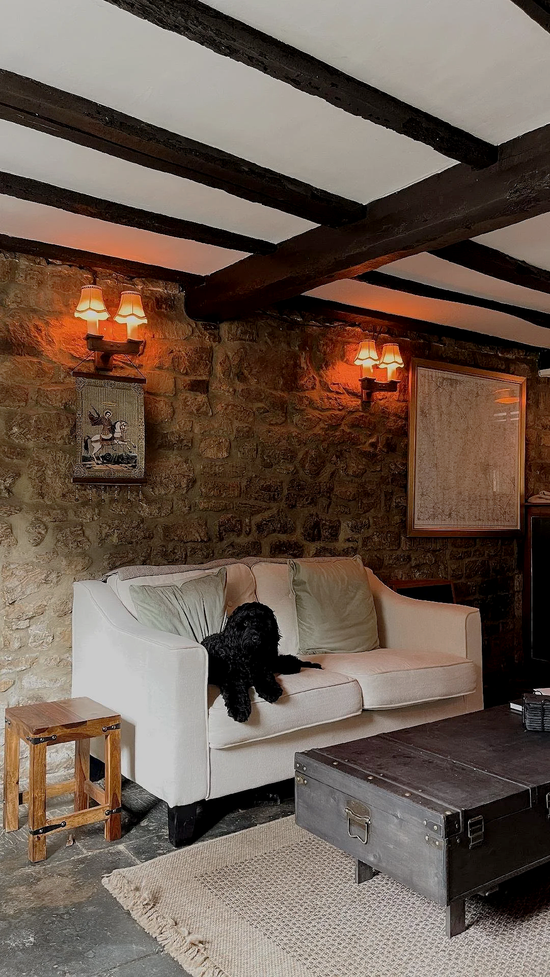A cosy pub lounge area in The Dun Cow featuring a white sofa, exposed stone walls, timber beams and warm ambient lighting.