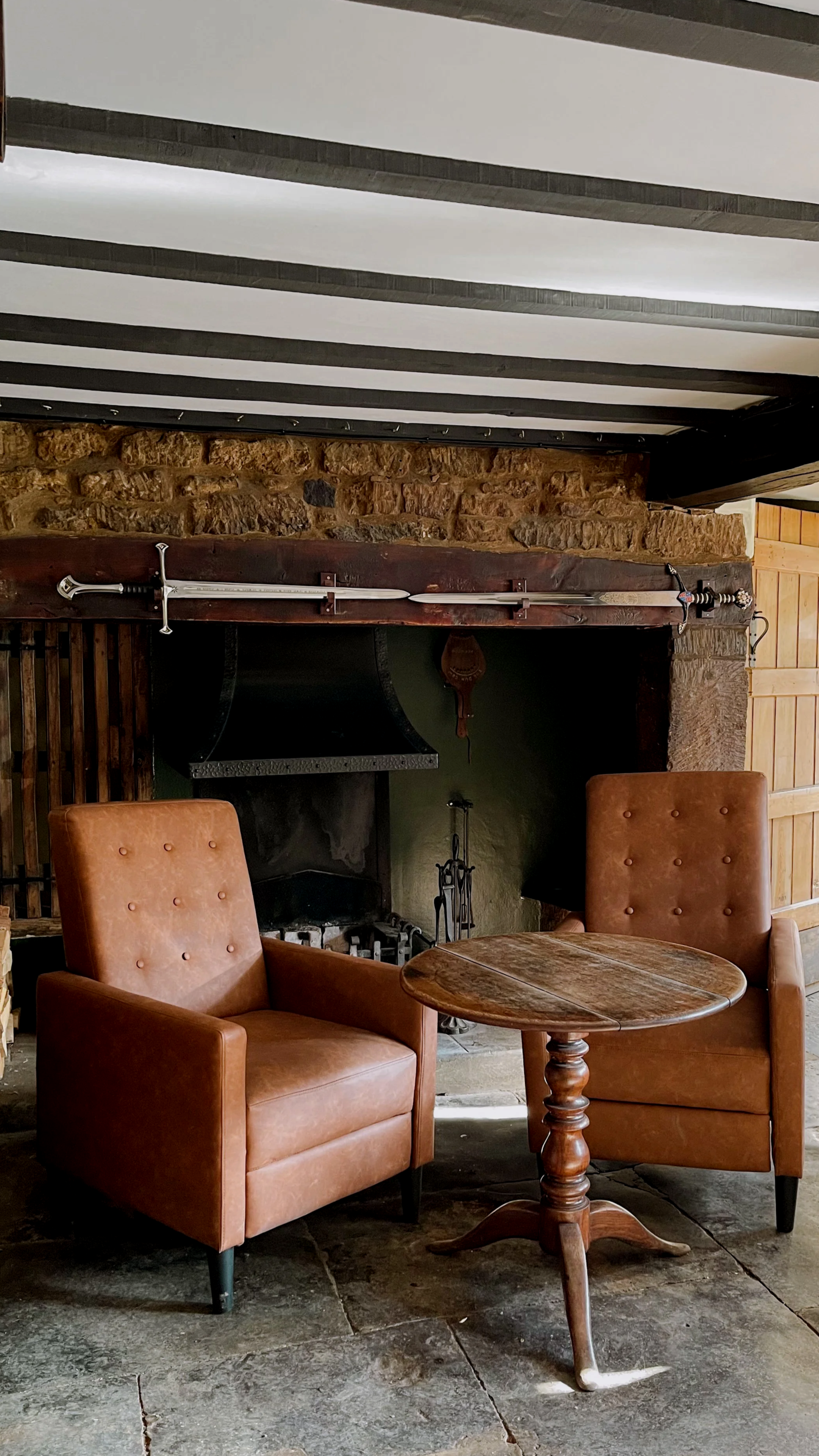 A cosy bar seating area in The Dun Cow with leather upholstered armchairs, beneath exposed dark wooden ceiling beams.