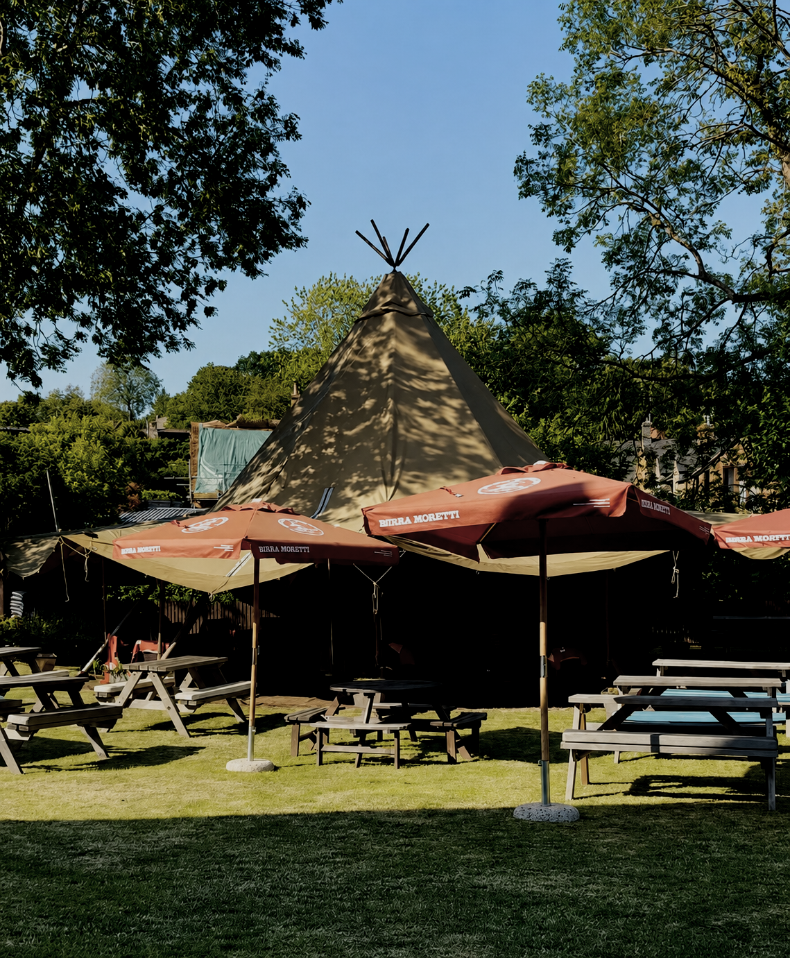 Outdoor beer garden area at The Dun Cow in Hornton, featuring picnic tables, outdoor seating, parasols and surrounding trees.