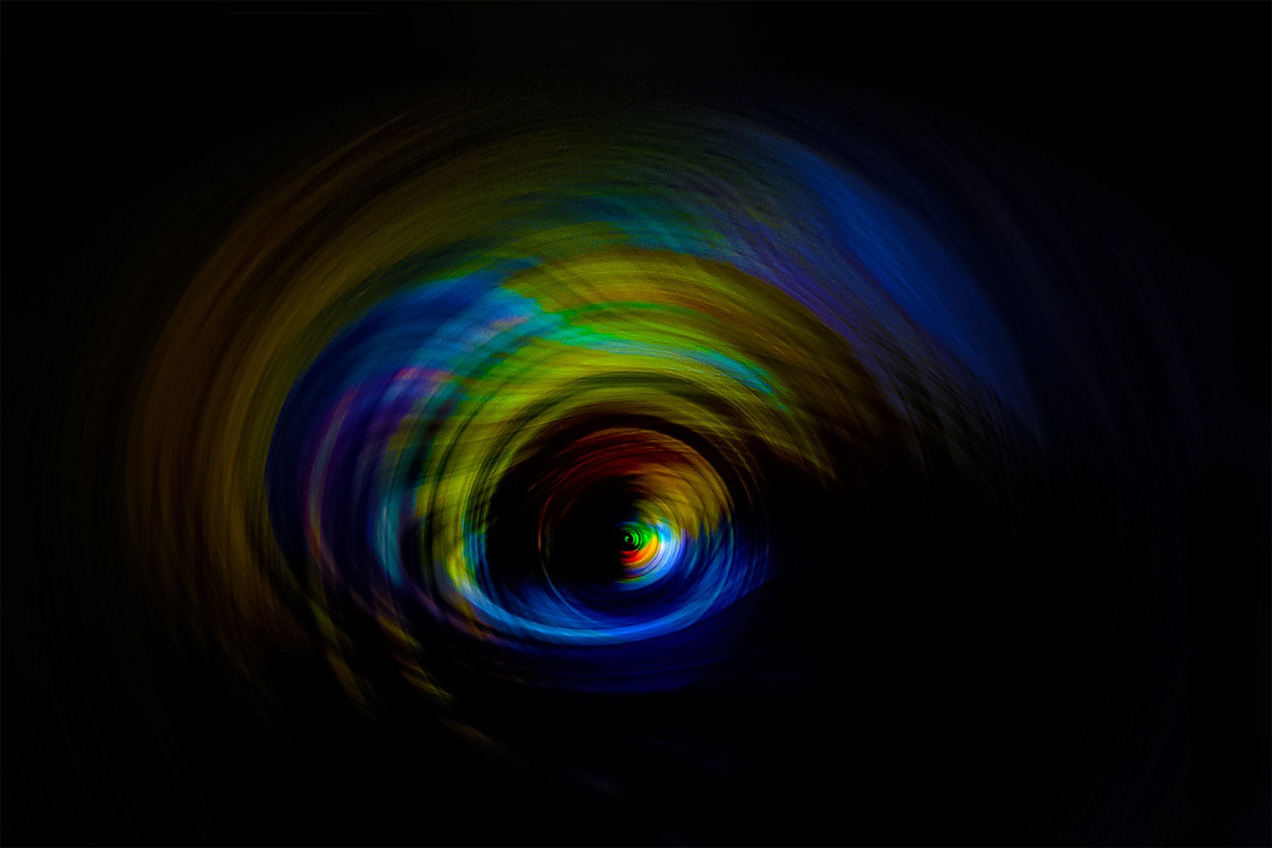 Colorful abstract spiral pattern with neon hues, resembling a vortex or tunnel in darkness.