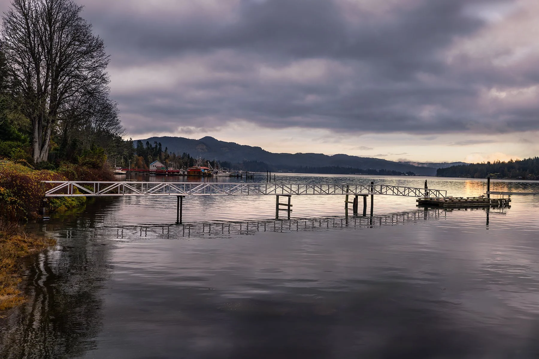 Scenic lake with a dock, surrounded by trees, hills, and cloudy sky at sunset.