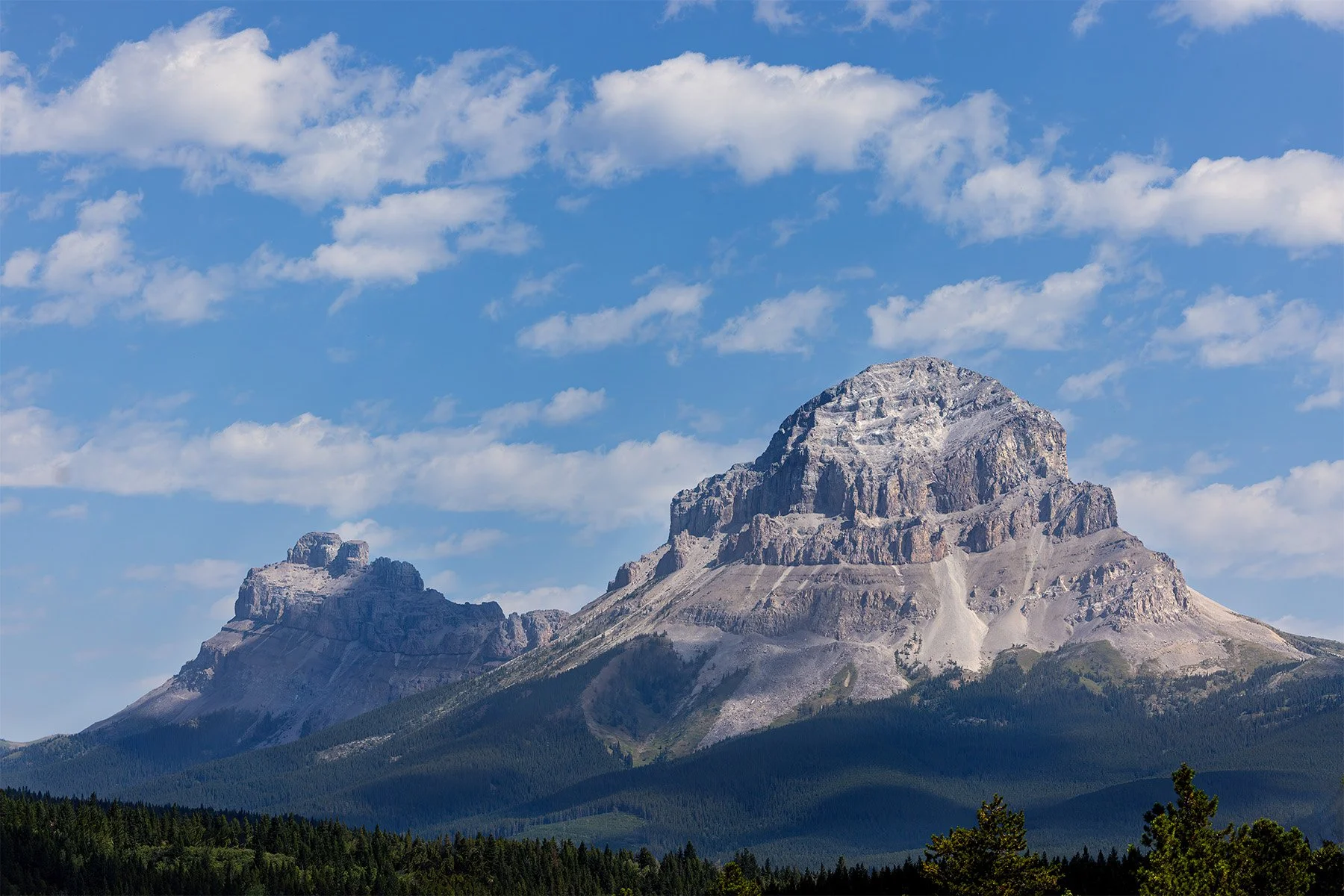 Scenic view of Castle Mountain in the Canadian Rockies under a blue sky with scattered clouds.
