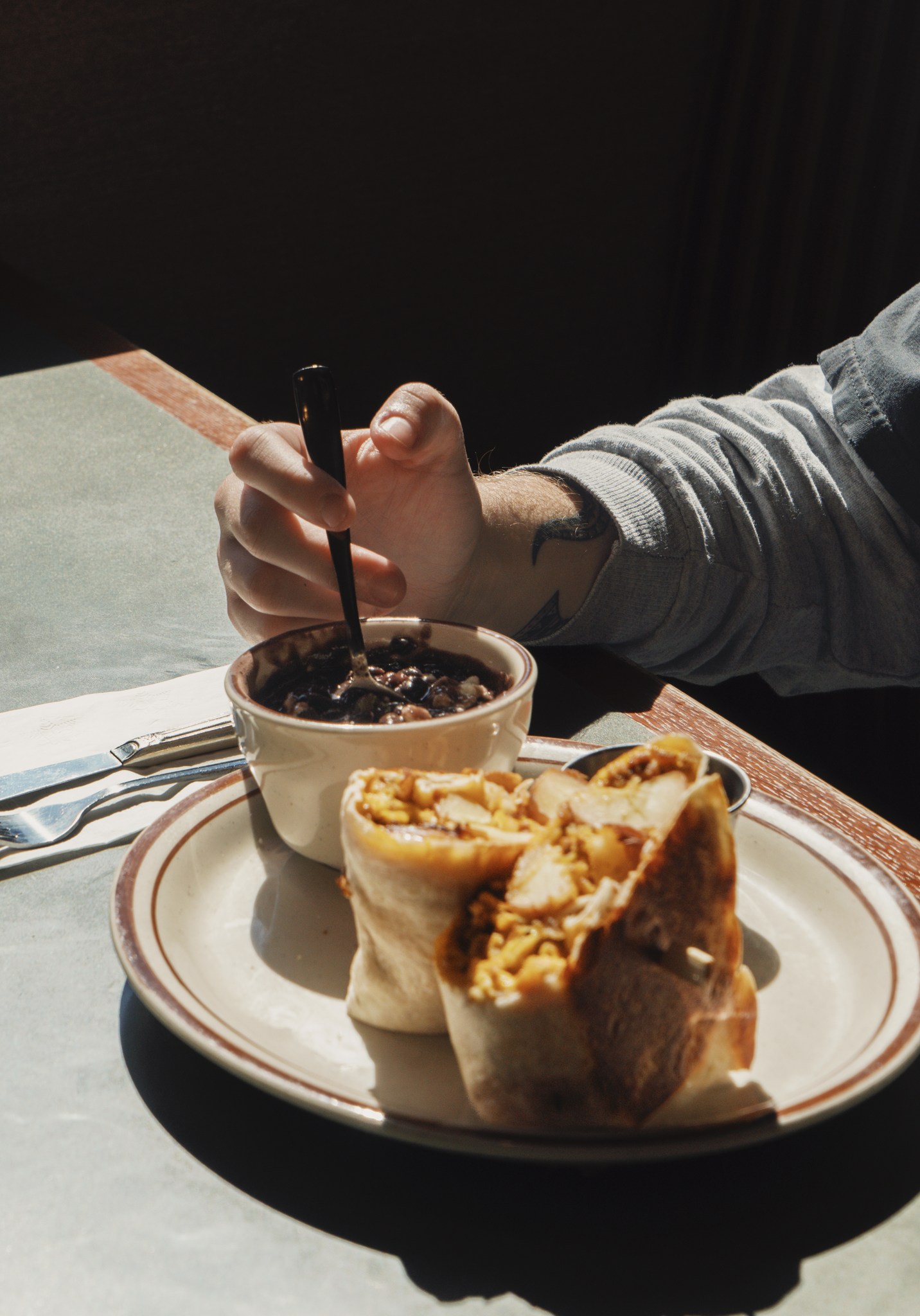 A person scooping up a spoonful of stewed black beans, served with a Chorizo Breakfast Burrito.