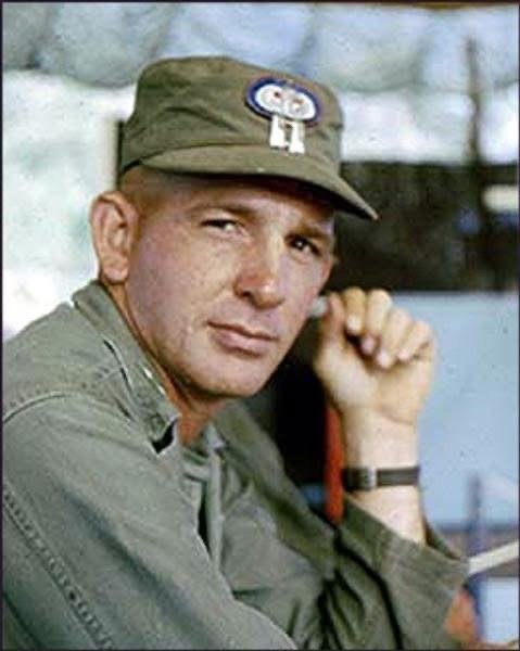 Man wearing military uniform and cap, seated and looking at camera.