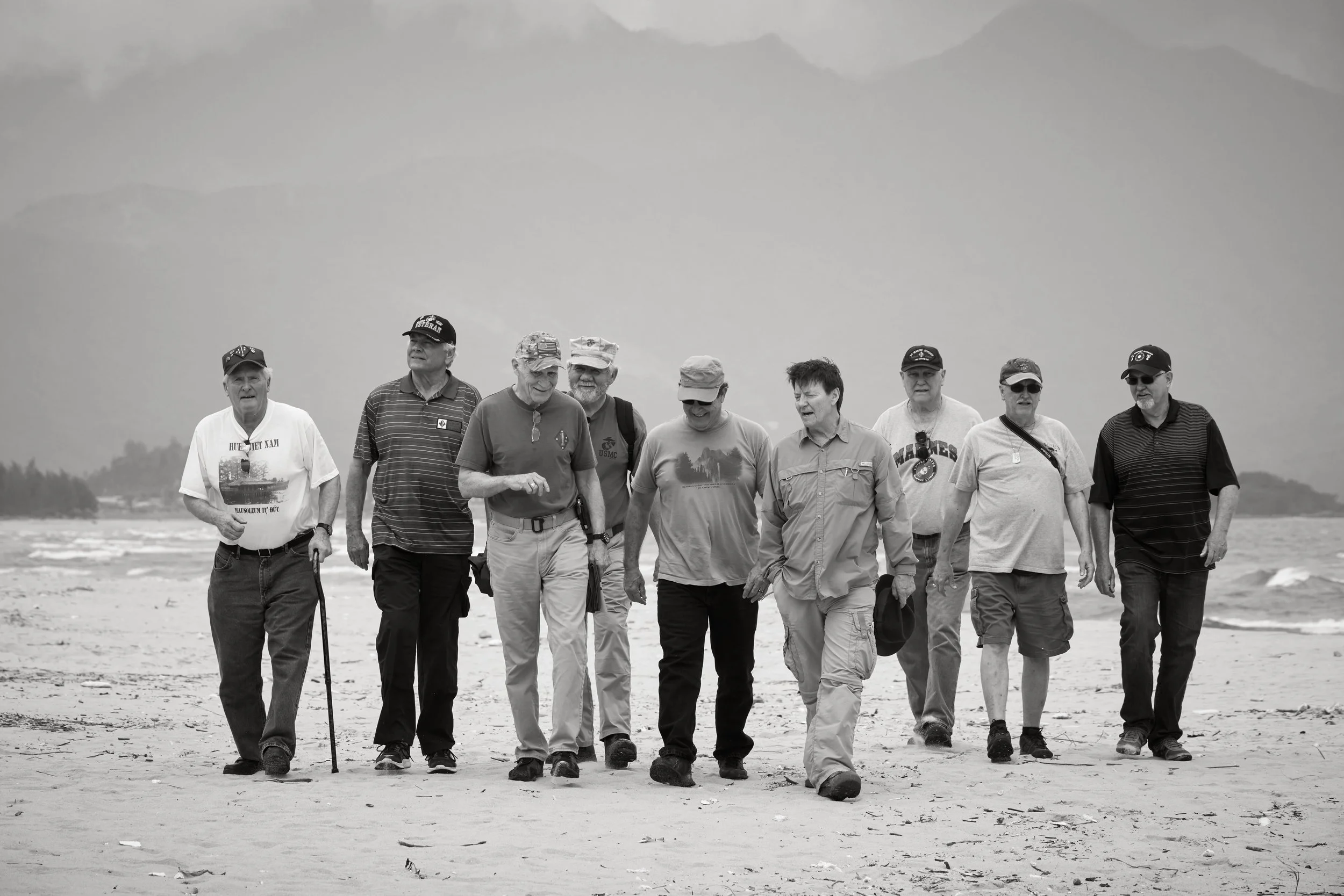 A group of ten men walking on a beach with mountains in the background.
