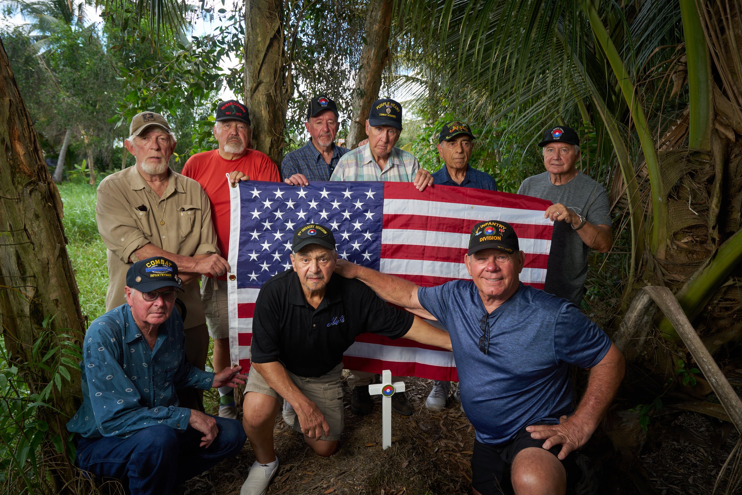 Group of men wearing military hats holding an American flag in a forested area.