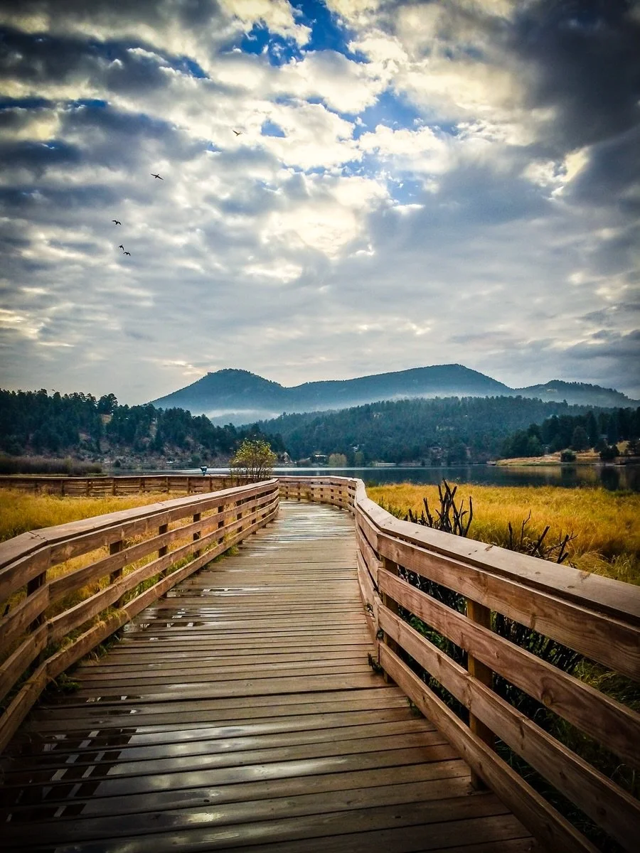 On the Boardwalk.
.
I captured this on a rainy fall morning at Evergreen Lake, one of my favorite places to walk in the early morning. I love the leading lines of the boardwalk, the feeling of peaceful solitude, and the glassy lake in the background.