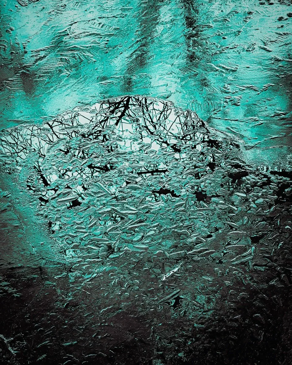 Beneath the Ice
.
Walking along a frozen pond, I almost passed it by&hellip;until the ice stopped me.

Up close, tree trunk shadows sink beneath the surface while branch reflections thread through the fissures, caught between worlds. I framed the sce