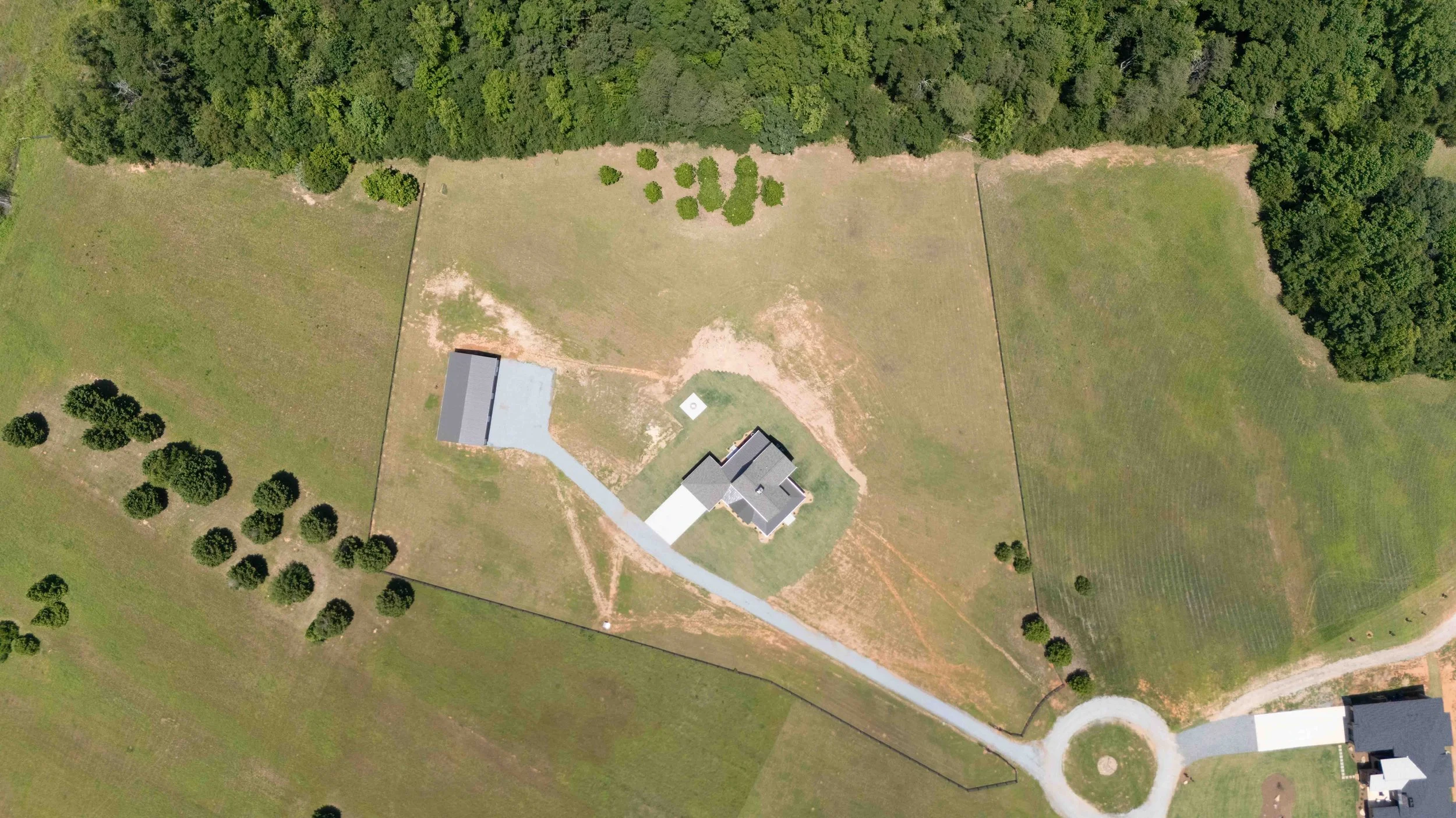Aerial view of a large property with a house, driveway, trees, open grassy areas, and a circular driveway entrance.