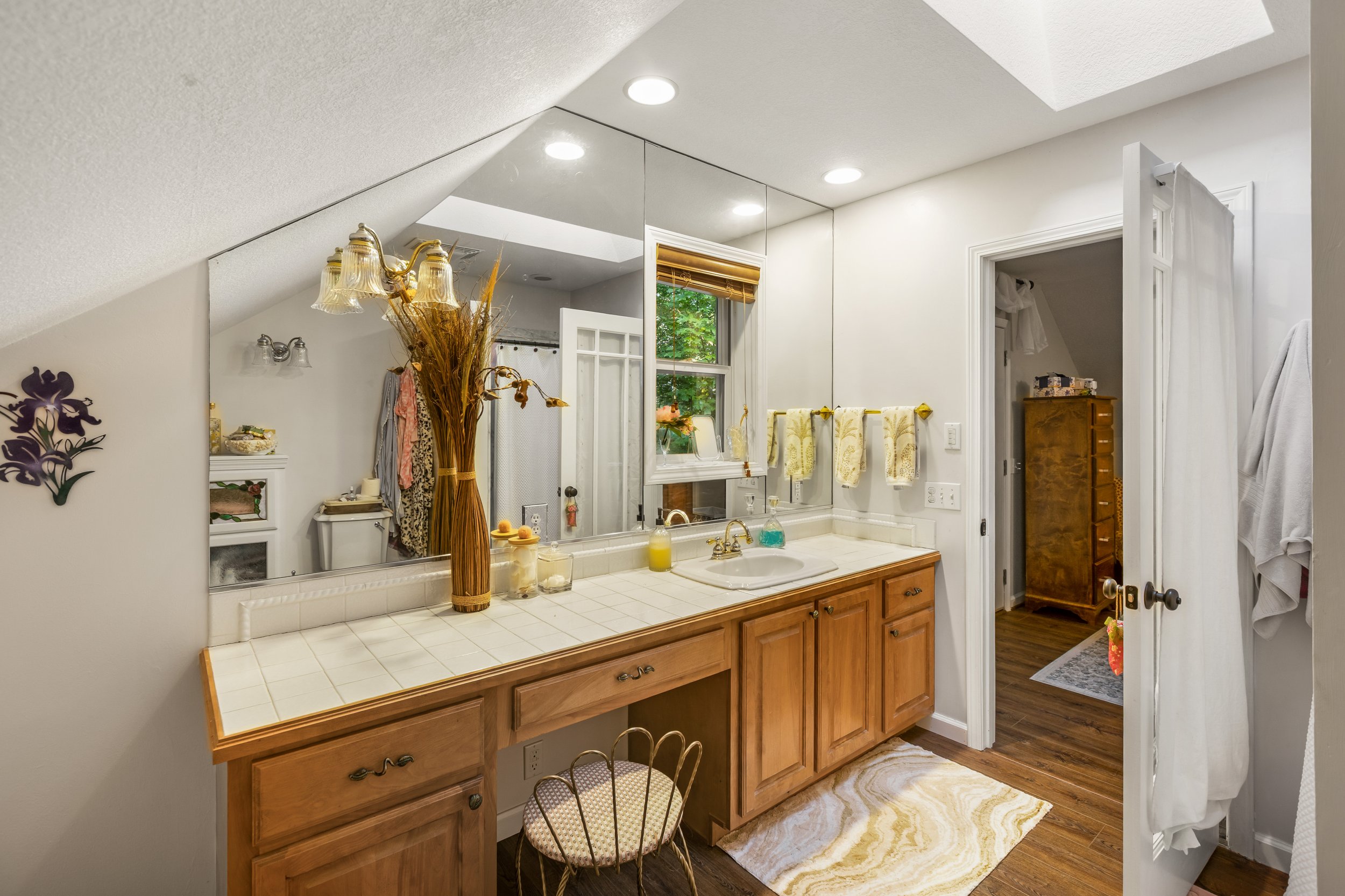A bathroom with a large mirror, wooden vanity, yellow towels, a window, and a white door leading to another room.